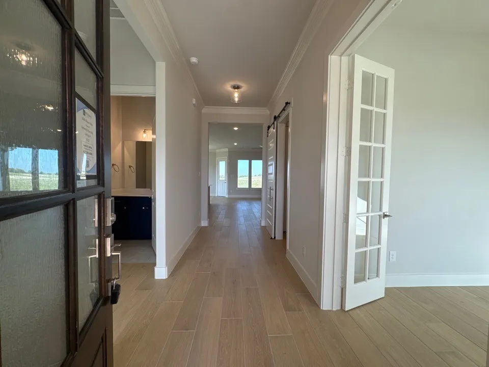 Entryway featuring wood-finish flooring, crown molding, a dark wood-paneled door with textured glass, and a barn door leading to a separate area