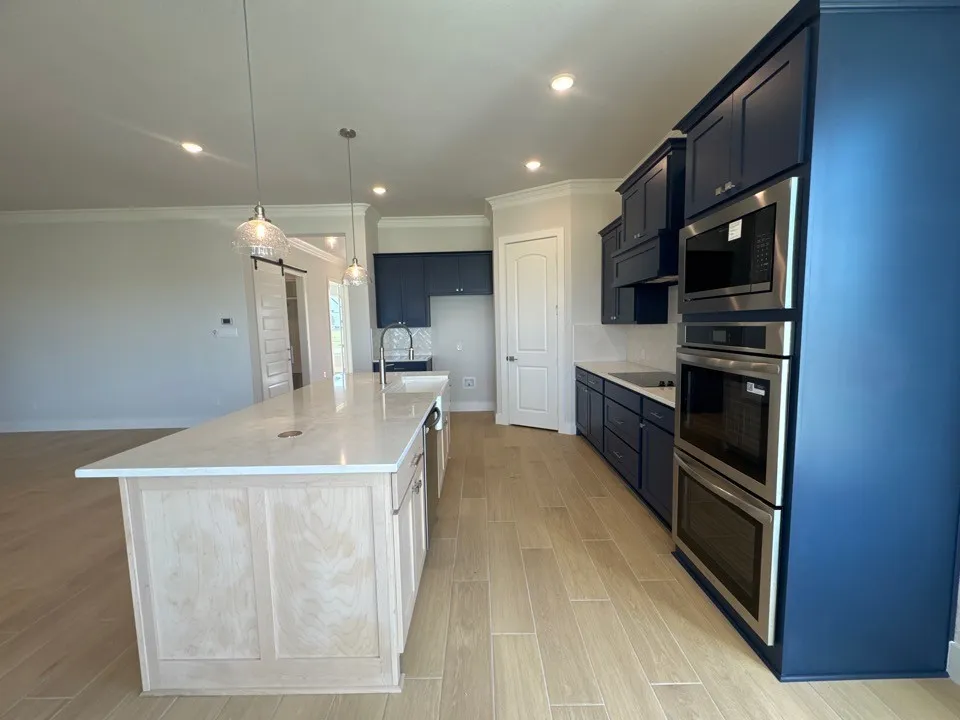 Kitchen featuring light wood-finish flooring, dark blue cabinetry, integrated stainless steel appliances, a center island with a light countertop, and clear pendant lighting