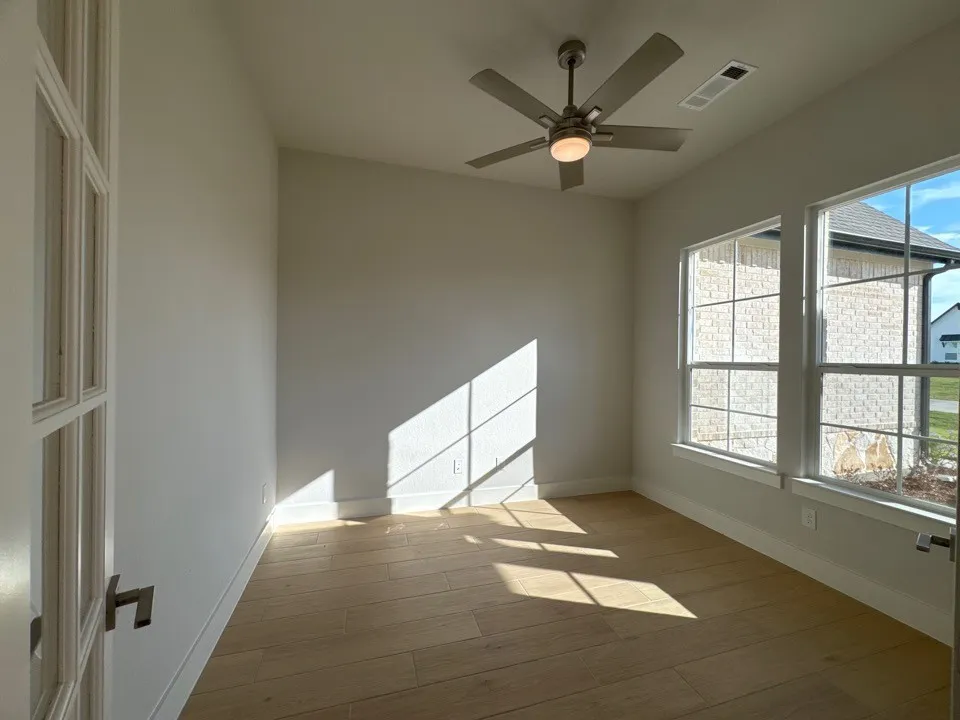 Wood-finish flooring, two large windows, white trim, and a ceiling fan with integrated lighting