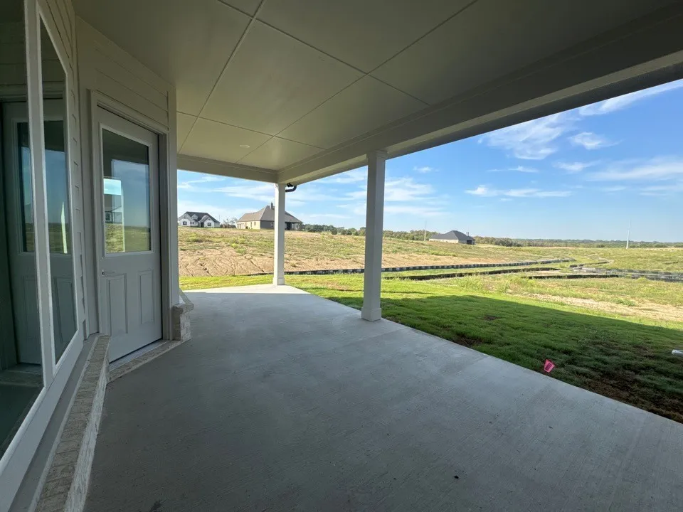 Covered concrete patio with white columns and a partial glass door