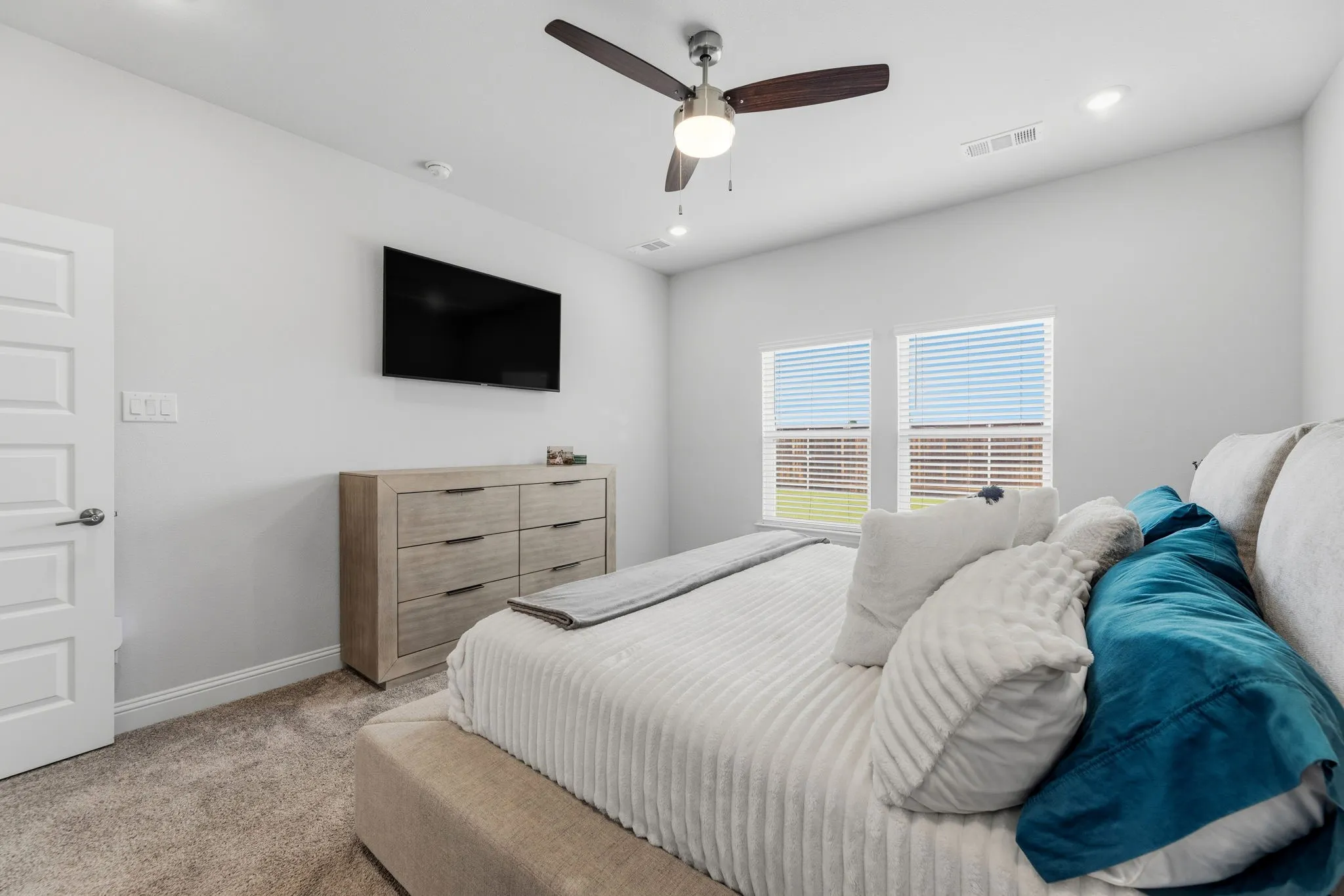 Carpeted bedroom featuring two windows with horizontal blinds, a ceiling fan with integrated lighting, recessed lighting, and a white paneled door