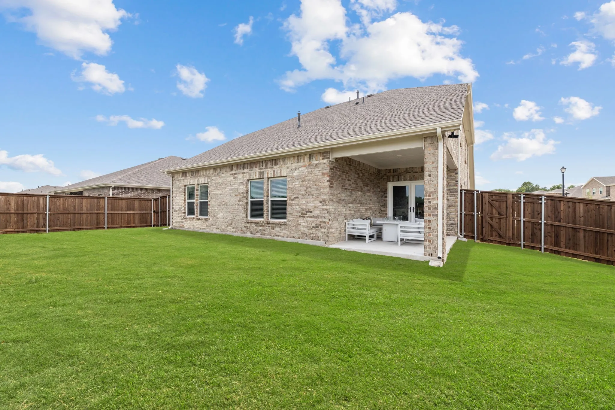 Expansive green lawn with a covered concrete patio featuring brick columns