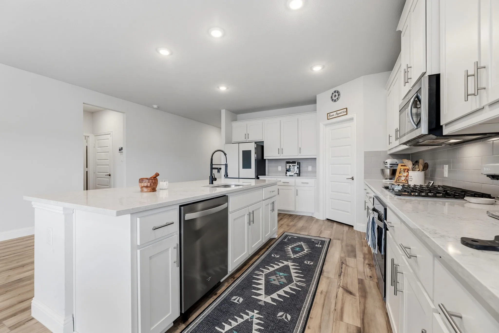 Spacious kitchen featuring an expansive center island with integrated stainless steel appliances, white cabinetry, and recessed lighting