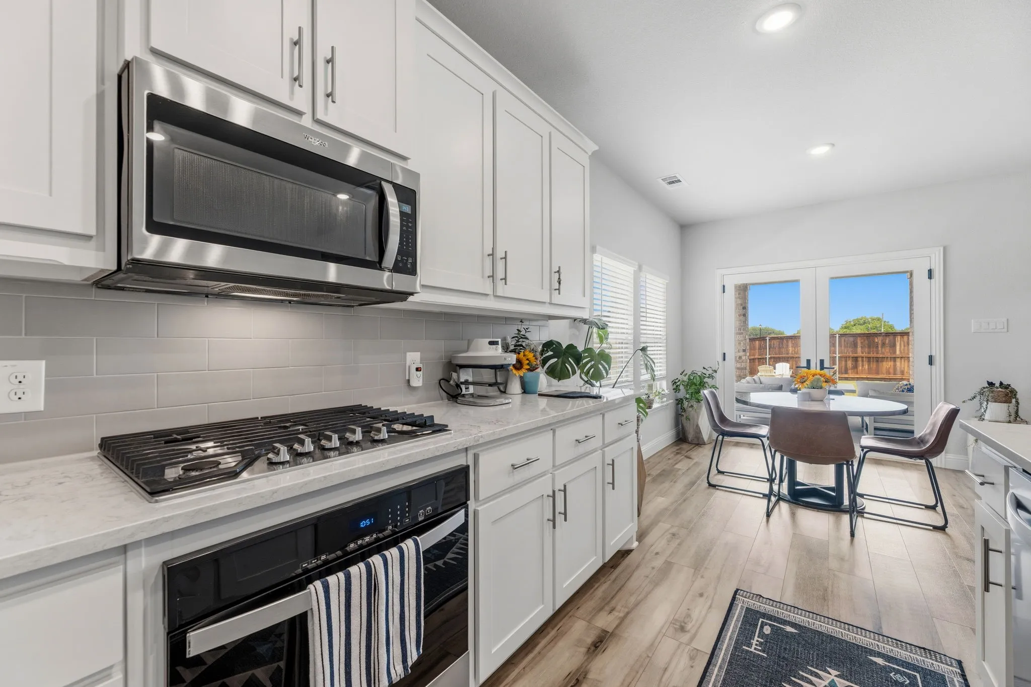 Kitchen featuring light-finish cabinetry, stainless steel microwave, gas range with an oven, light-toned countertops, and a gray subway tile backsplash