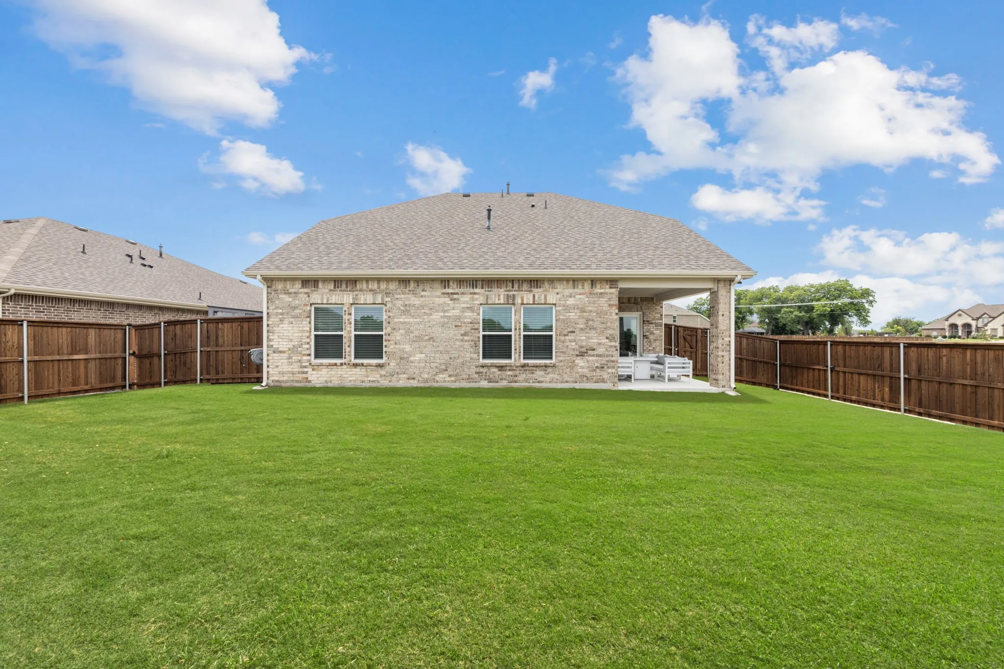 Expansive green lawn with a covered patio, brick exterior, and a privacy fence