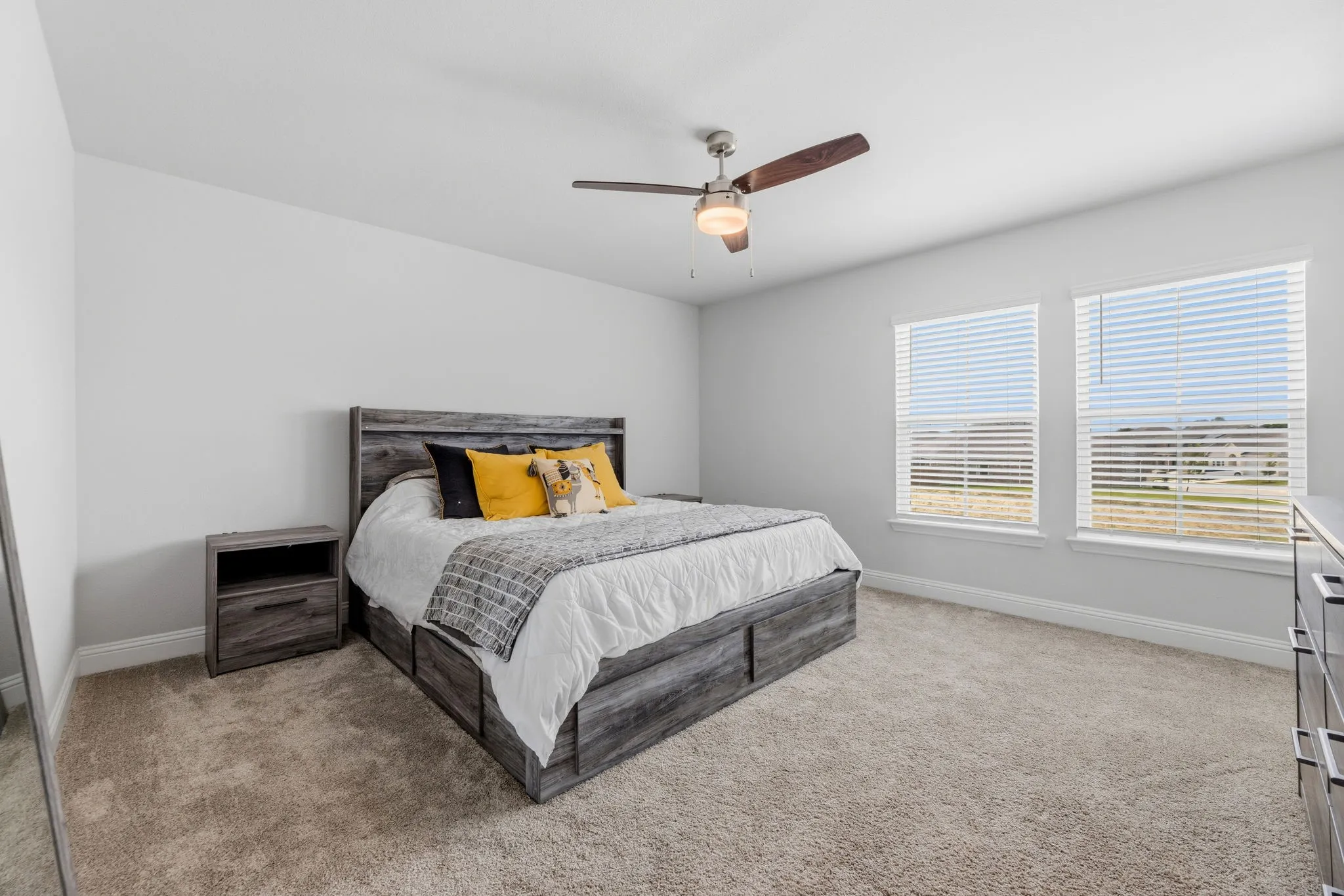 Carpeted bedroom featuring a ceiling fan with integrated lighting, two windows with horizontal blinds, and neutral wall paint