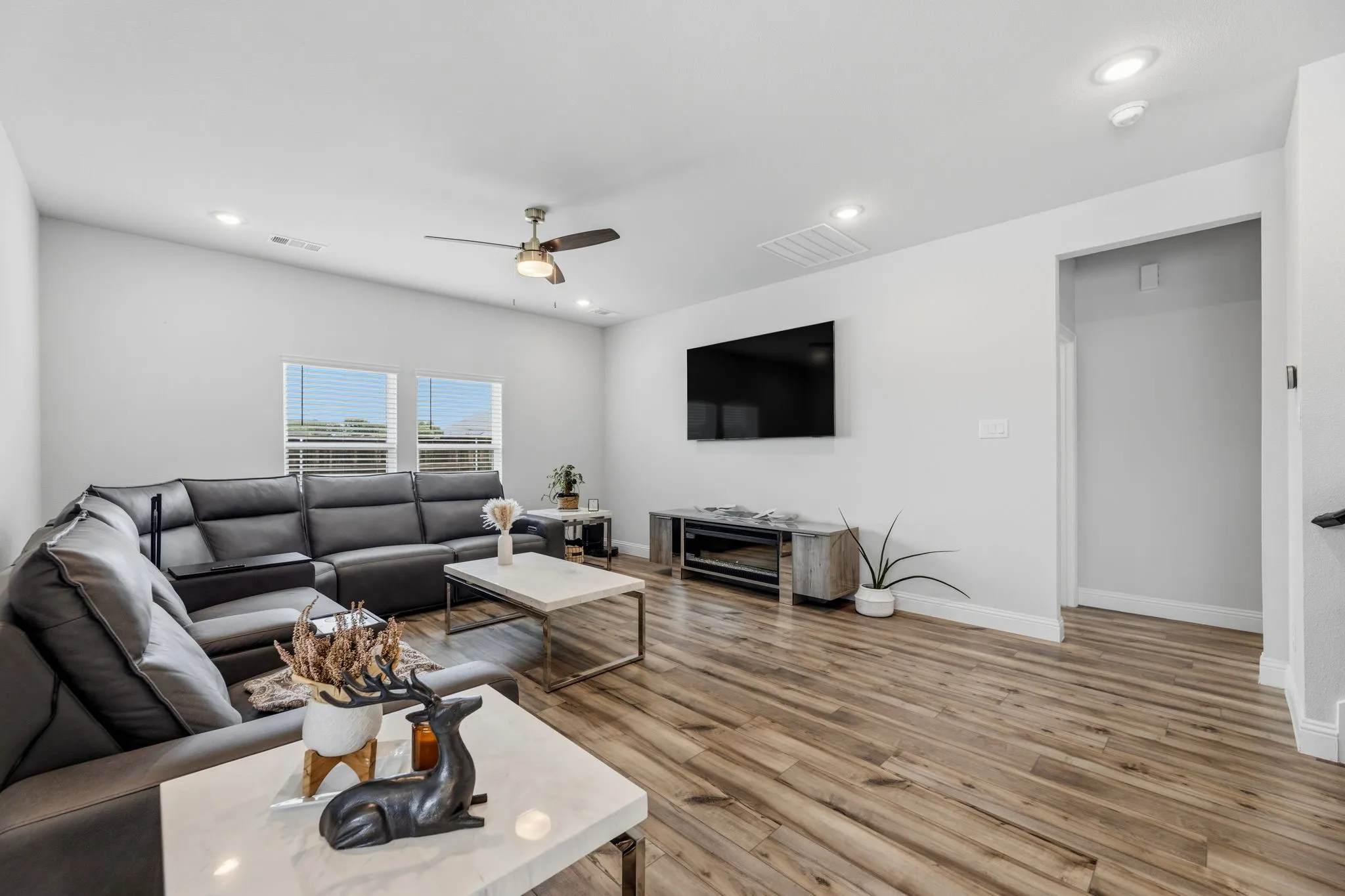 Spacious living area featuring wood-finish flooring, recessed lighting, ceiling fan with light fixture, and white trim