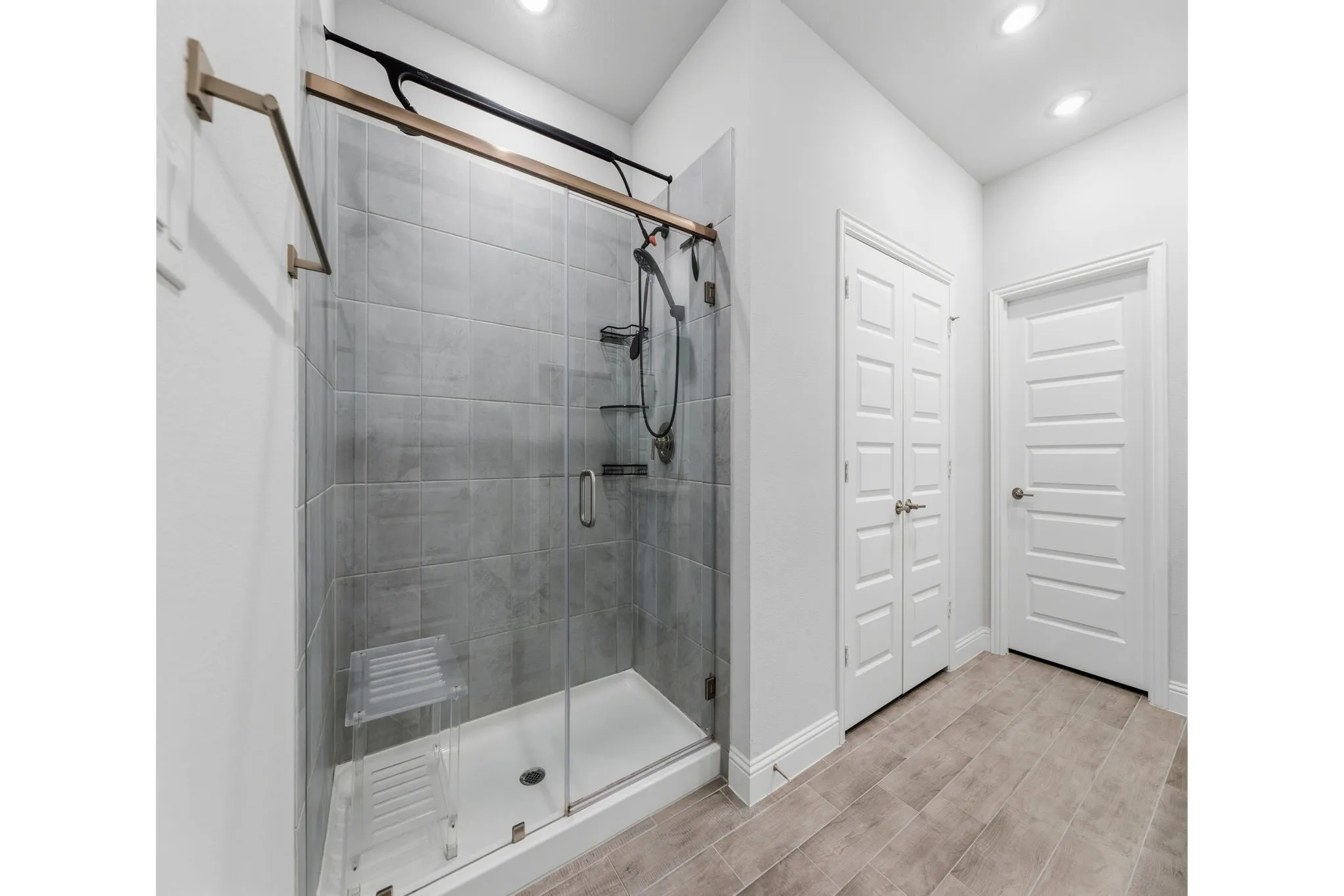 Frameless glass shower enclosure with subway tile surround, matte black fixtures, and a white shower pan