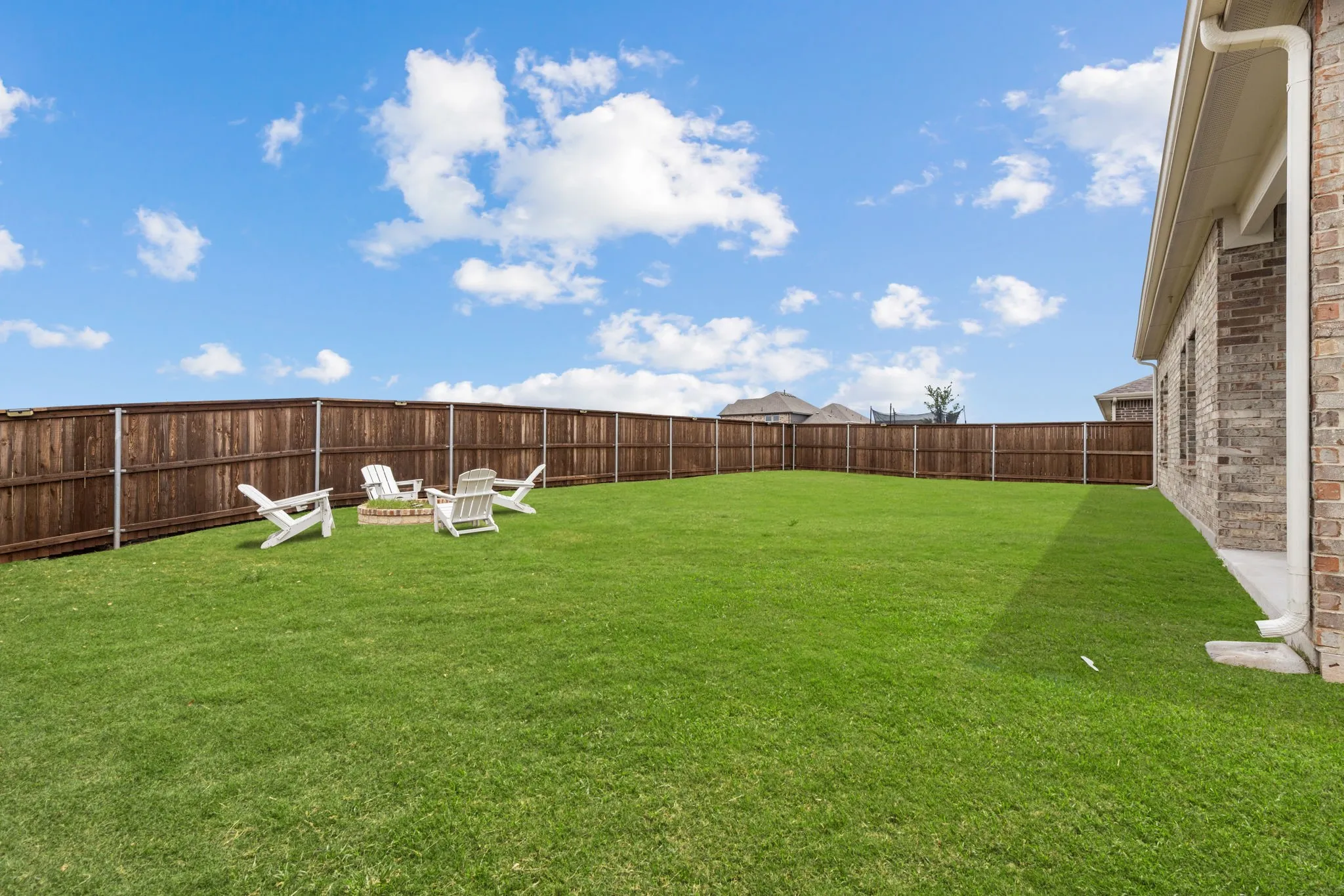 Spacious backyard featuring a full wood privacy fence, expansive green lawn, and a built-in fire pit