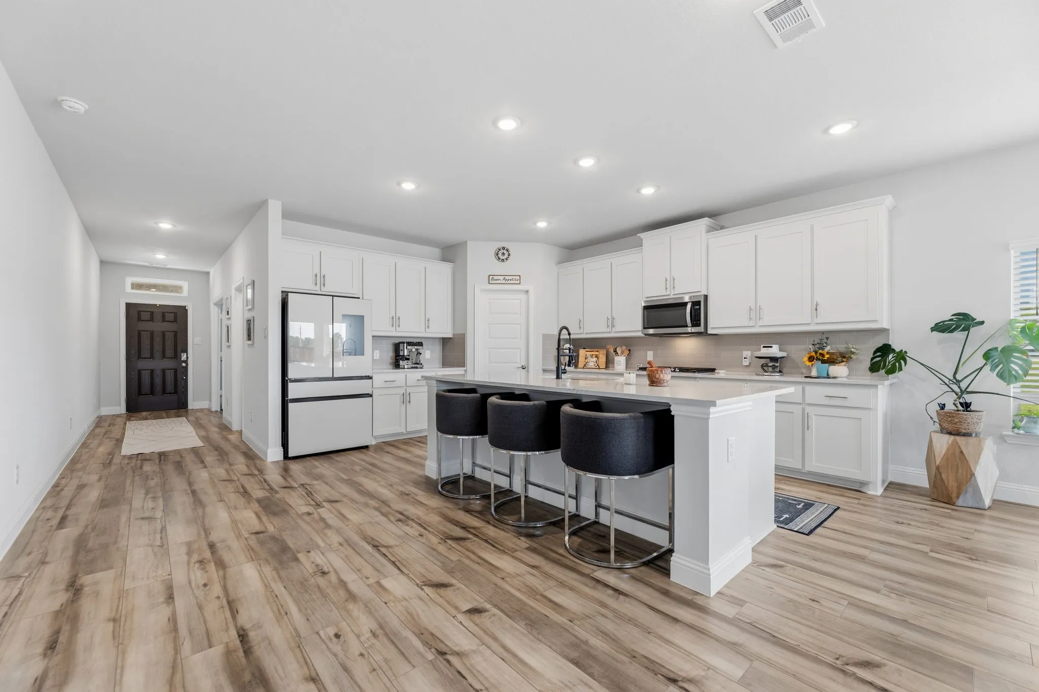 Open-concept kitchen featuring an oversized island with seating, white shaker cabinetry, stainless steel appliances, and wood-finish flooring