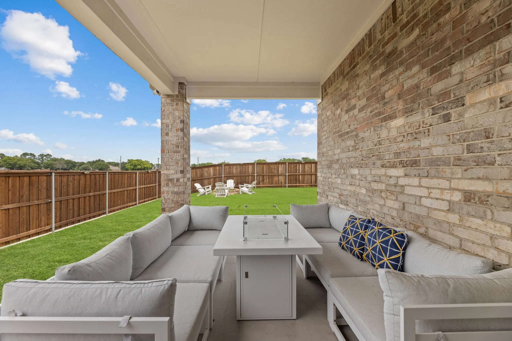Covered patio featuring a brick accent wall, stone column, concrete flooring, and an expansive lawn