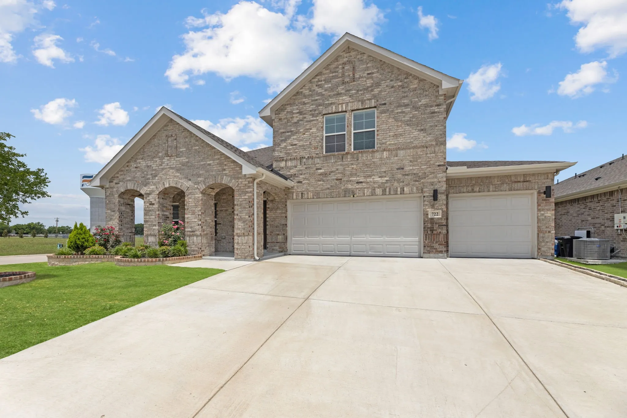 Two-story brick exterior featuring a multi-car driveway, arched entryway, and a landscaped front yard with a manicured lawn