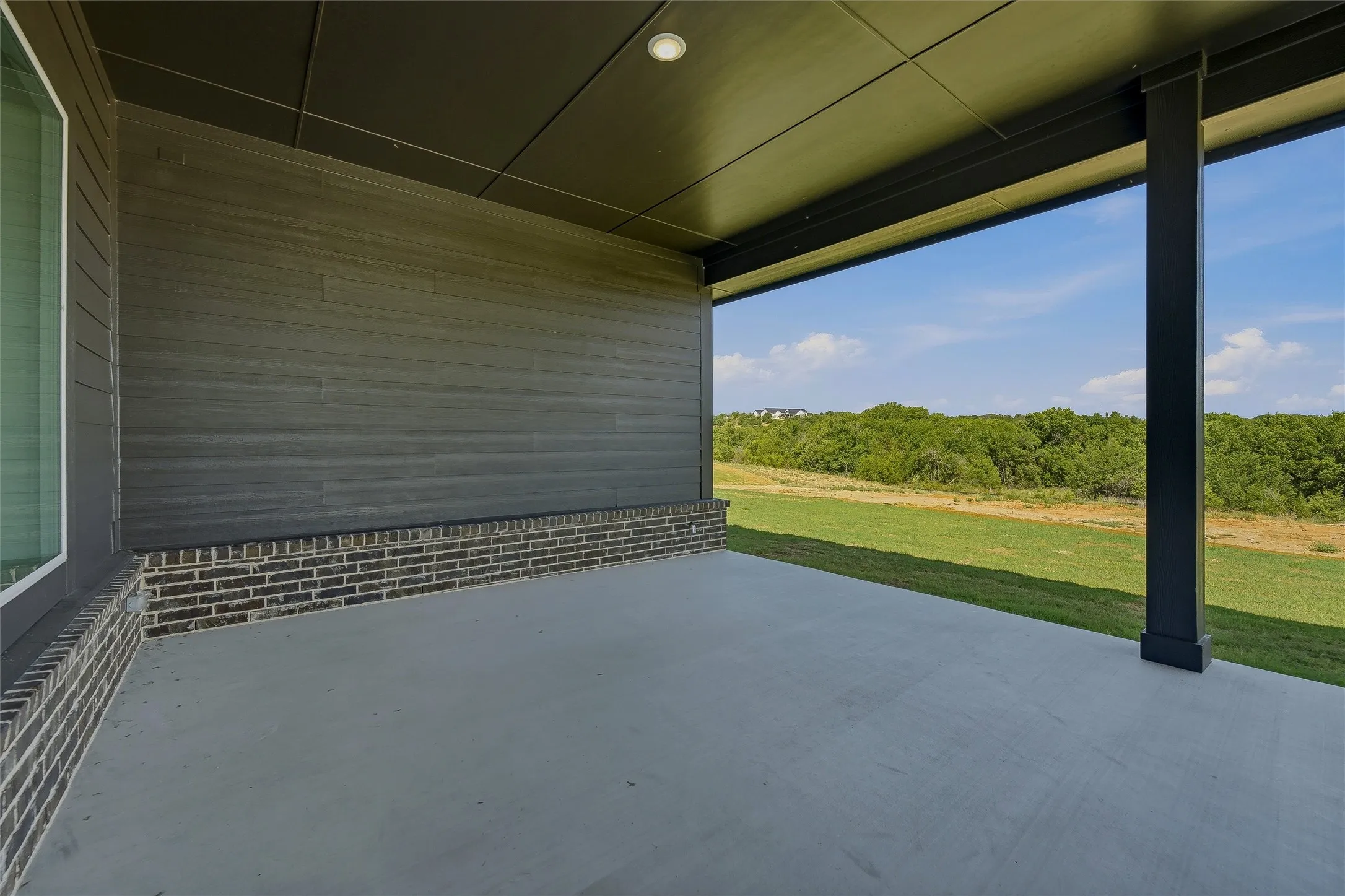 Covered patio featuring a concrete slab, dark brick base, and horizontal wood-finish siding