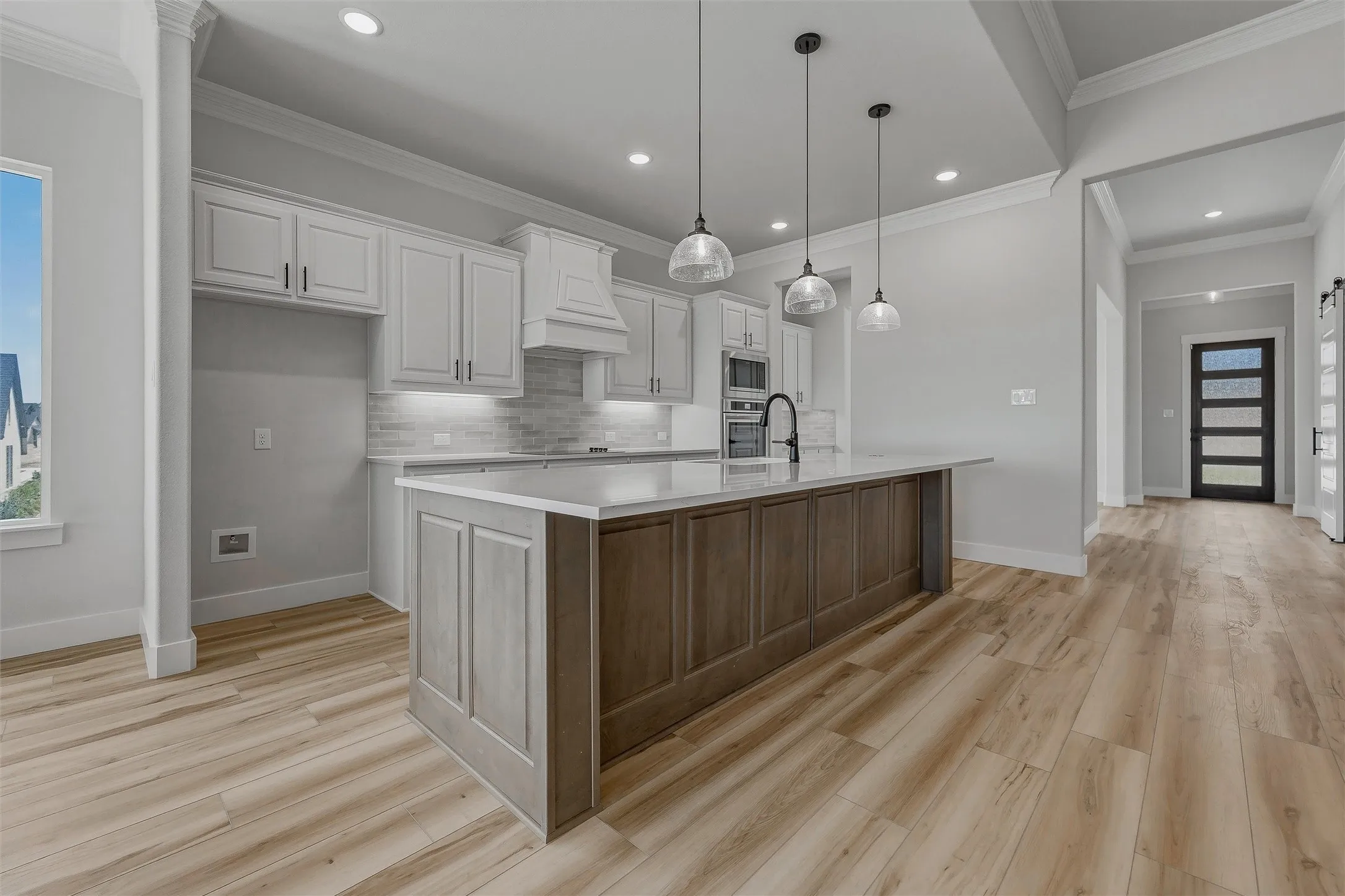 Kitchen featuring a large island with paneling, pendant lighting, built-in appliances, and light-toned cabinetry