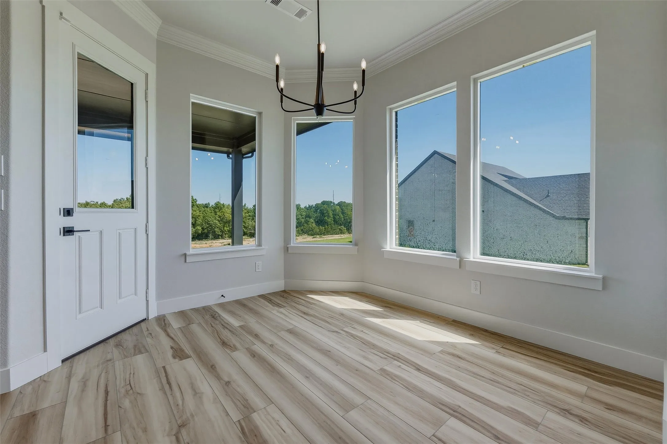Wood-finish flooring, multiple windows, crown molding, modern chandelier, and a white paneled door with matte black hardware