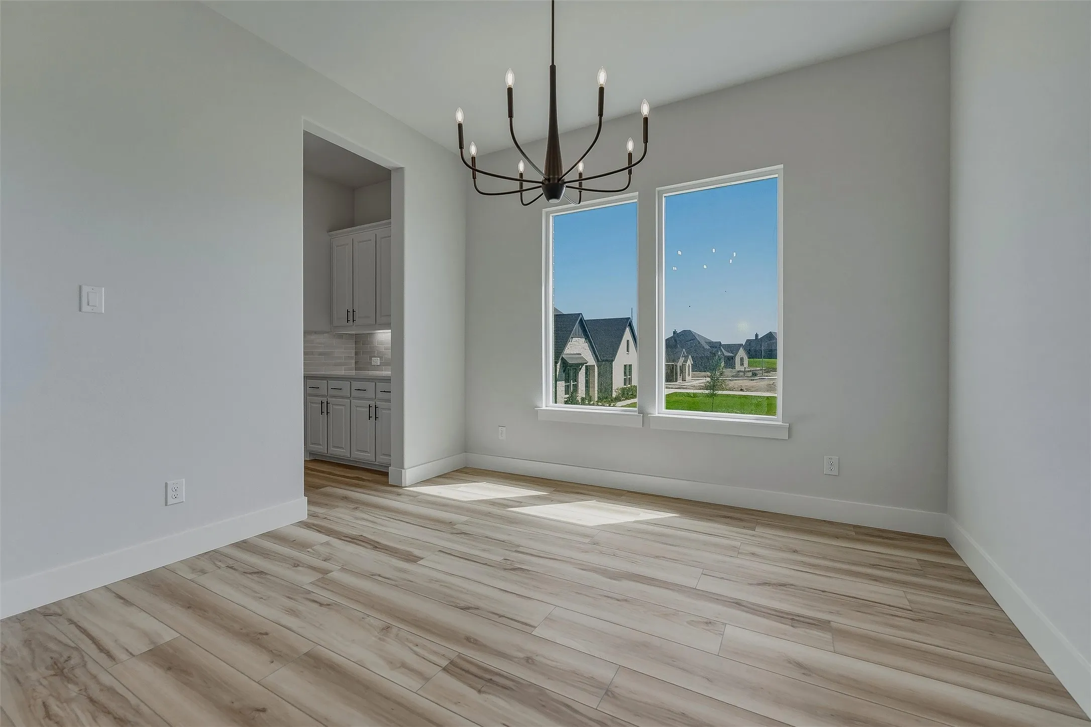 Spacious room featuring wood-finish flooring, a modern black chandelier, and two large windows