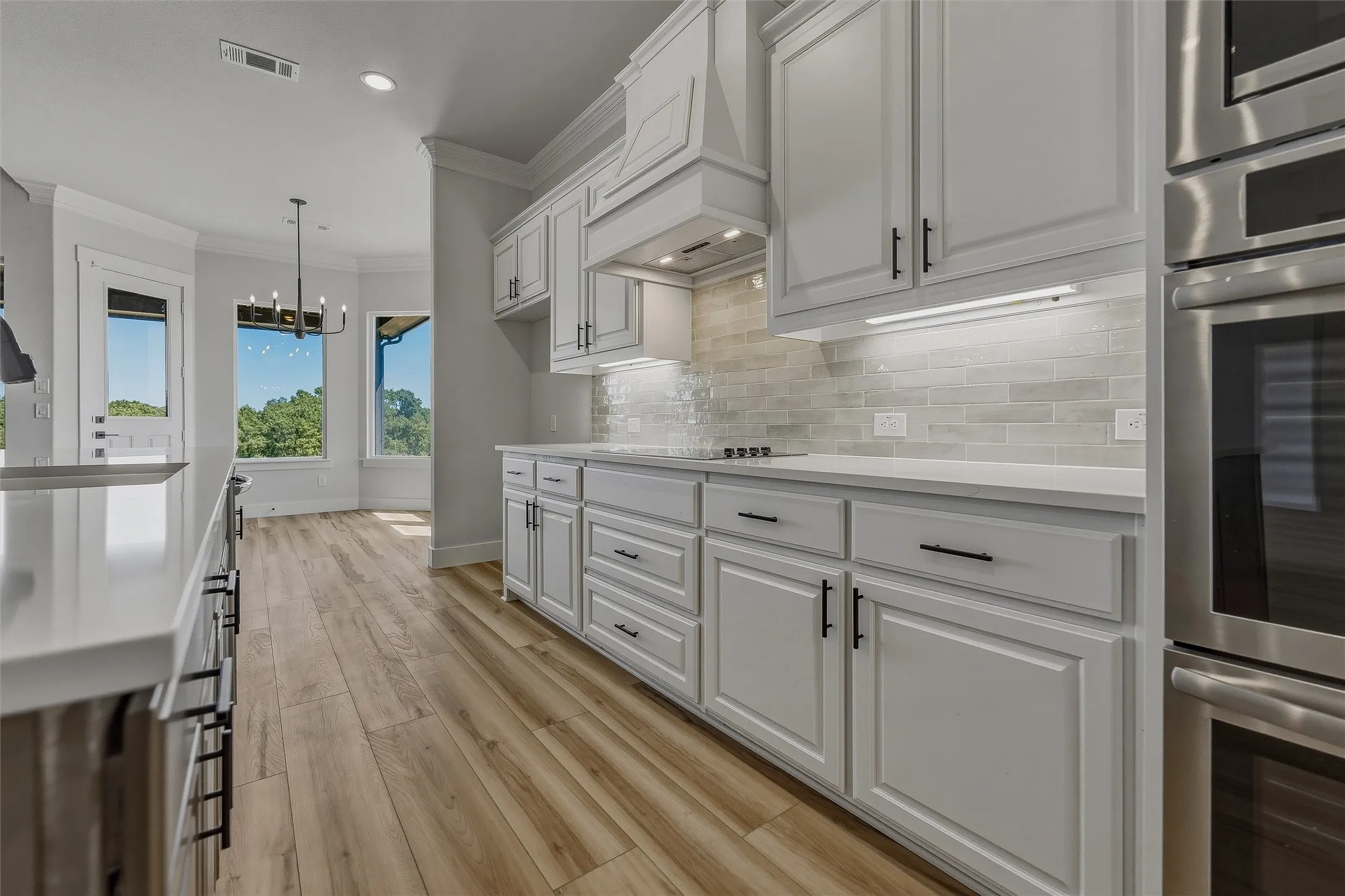 White cabinetry with black hardware, wood-finish flooring, light-toned tile backsplash, stainless steel appliances, and white countertops