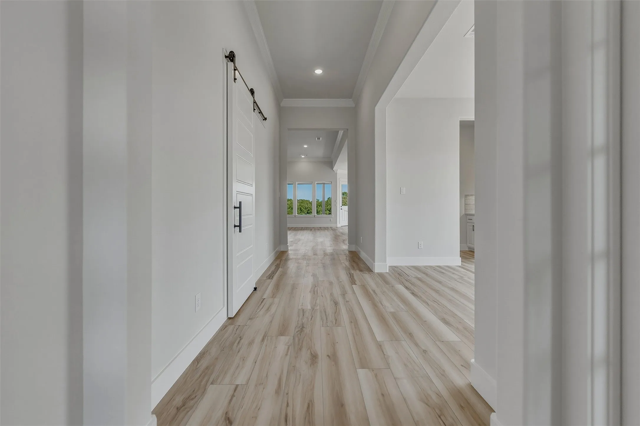Wood-finish flooring throughout, featuring a white barn door with black hardware, recessed lighting, and expansive windows offering a scenic backdrop