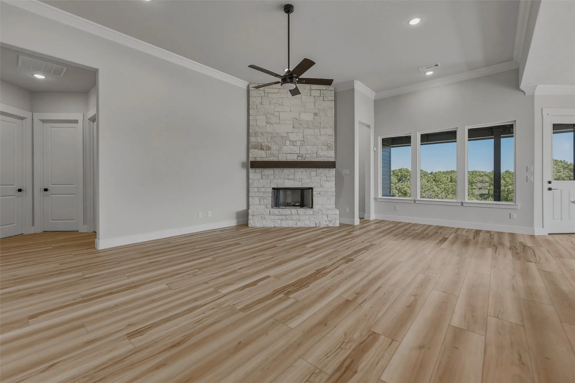 Spacious room featuring wood-finish flooring, a stone-clad fireplace with a wood mantle, a ceiling fan, vaulted ceilings, and large windows