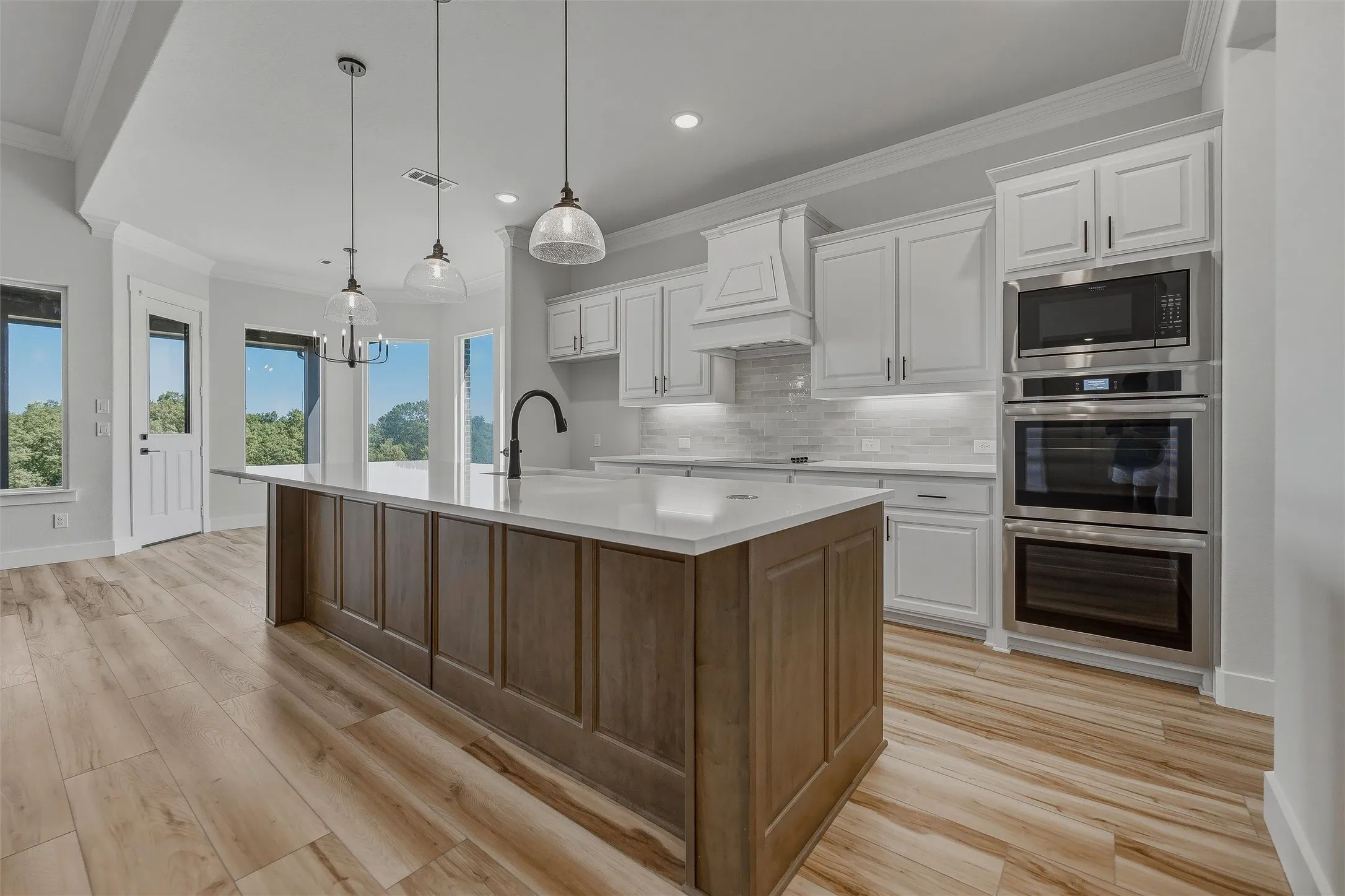 Kitchen with a large wood-finish island, white cabinetry, integrated stainless steel appliances, light-toned wood-finish flooring, and pendant lighting