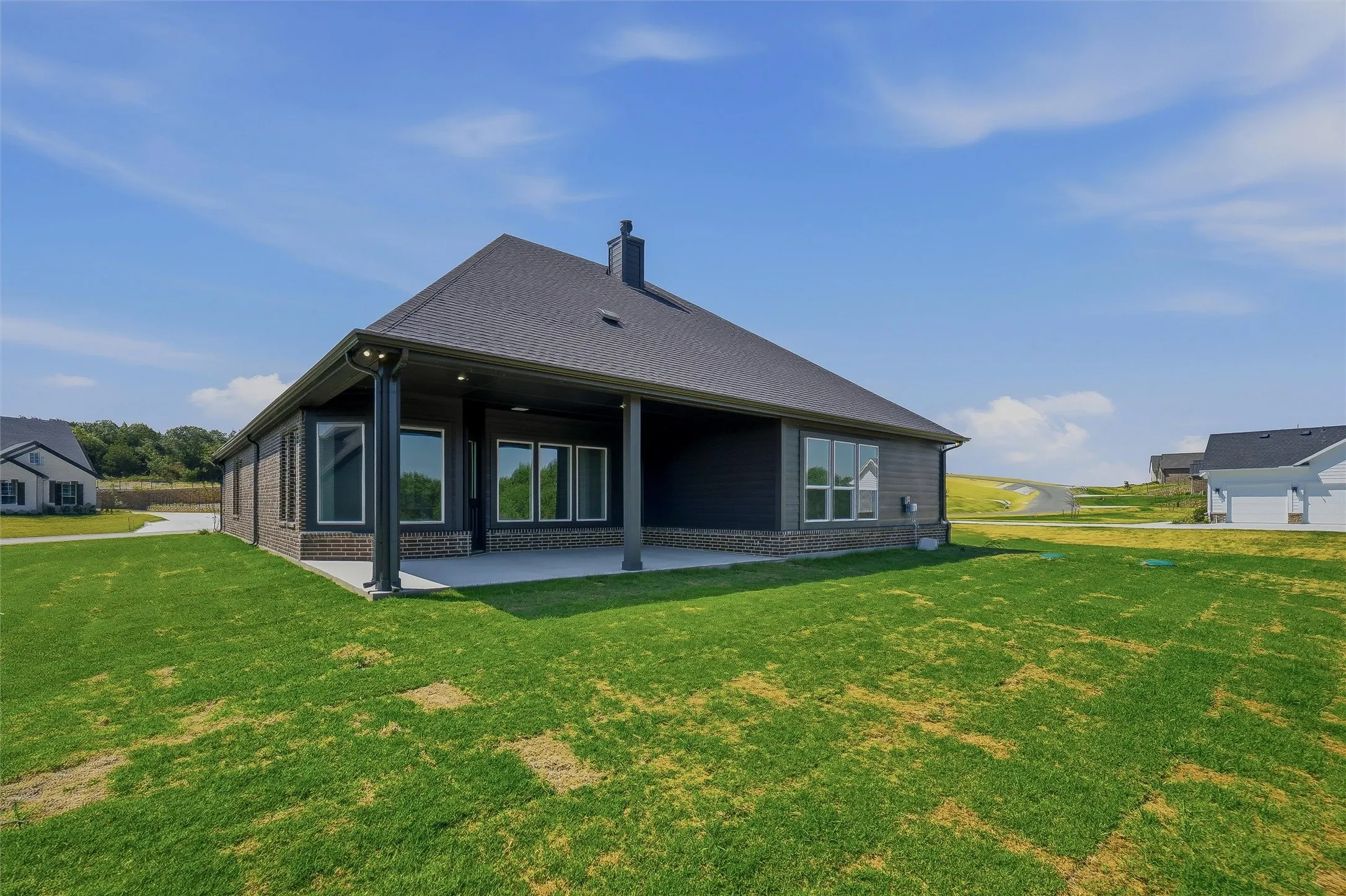 Exterior with a dark shingle roof, dark siding, and a covered patio supported by columns