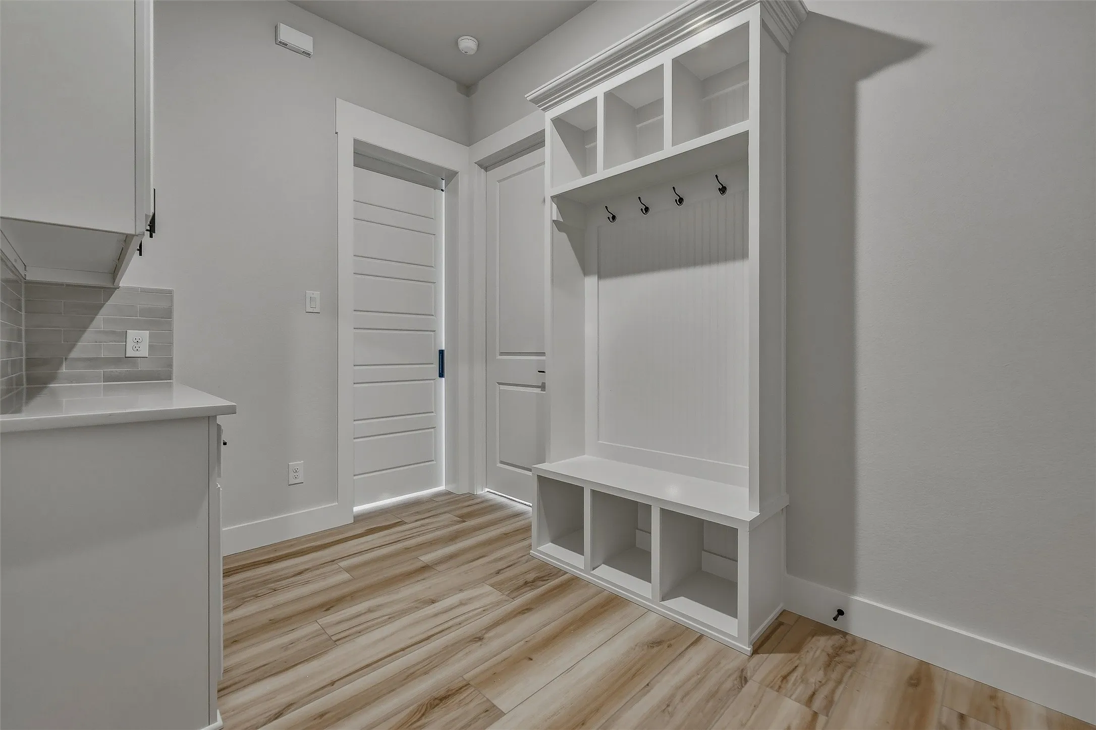 Built-in storage bench with cubbies, upper shelving, coat hooks, and wood-finish flooring