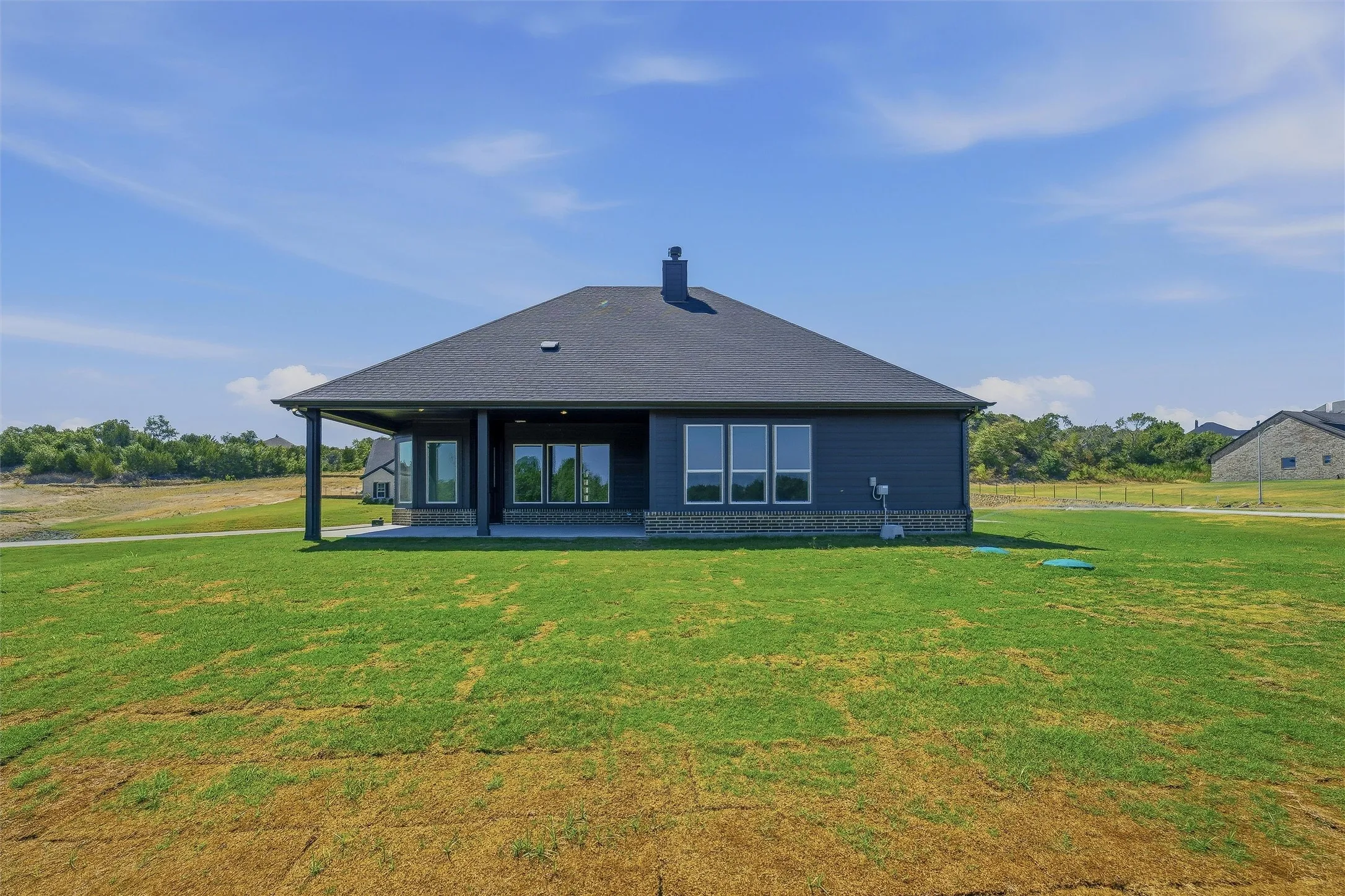 Expansive backyard with a covered patio, multiple large windows, dark siding, and a dark shingled roof