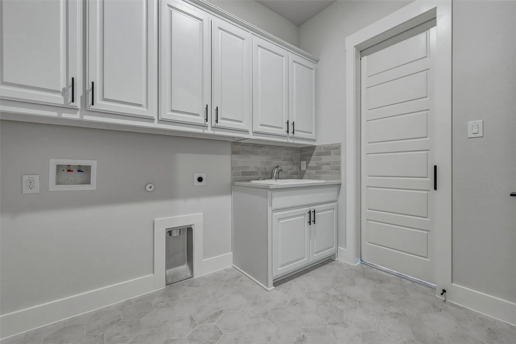 White cabinetry with matte black hardware, utility sink with tile backsplash, hexagonal floor tiles, and a five-panel interior door