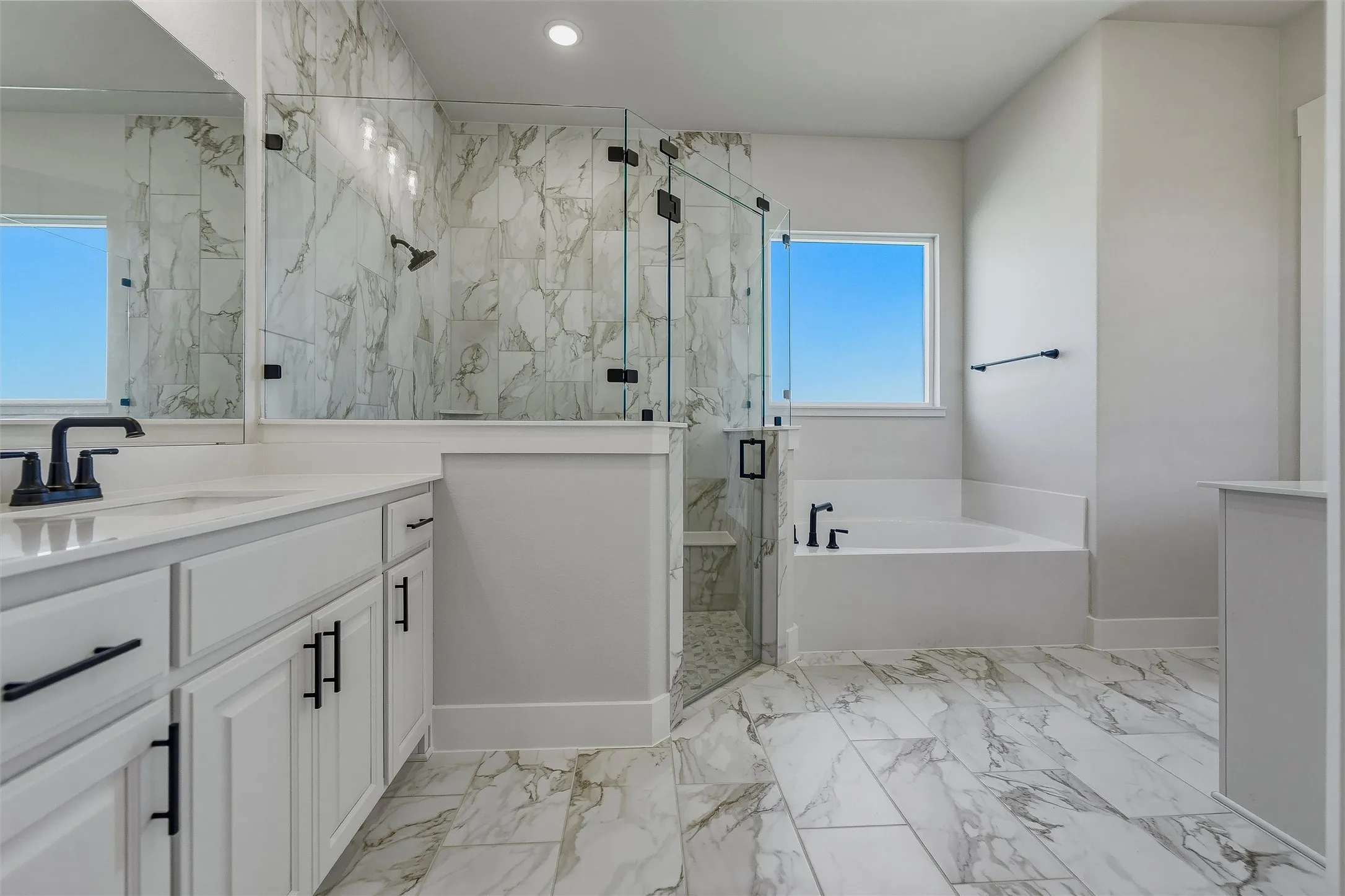 White vanity with a solid surface countertop, matte black fixtures, glass-enclosed shower with tile surround, and a built-in tub