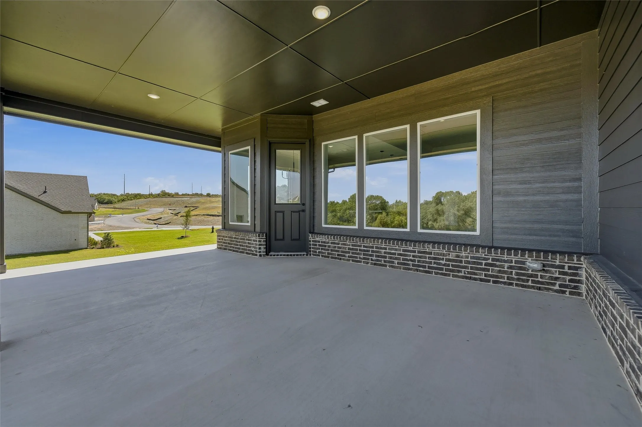 Spacious covered patio with concrete flooring, recessed lighting, and a dark brick foundation