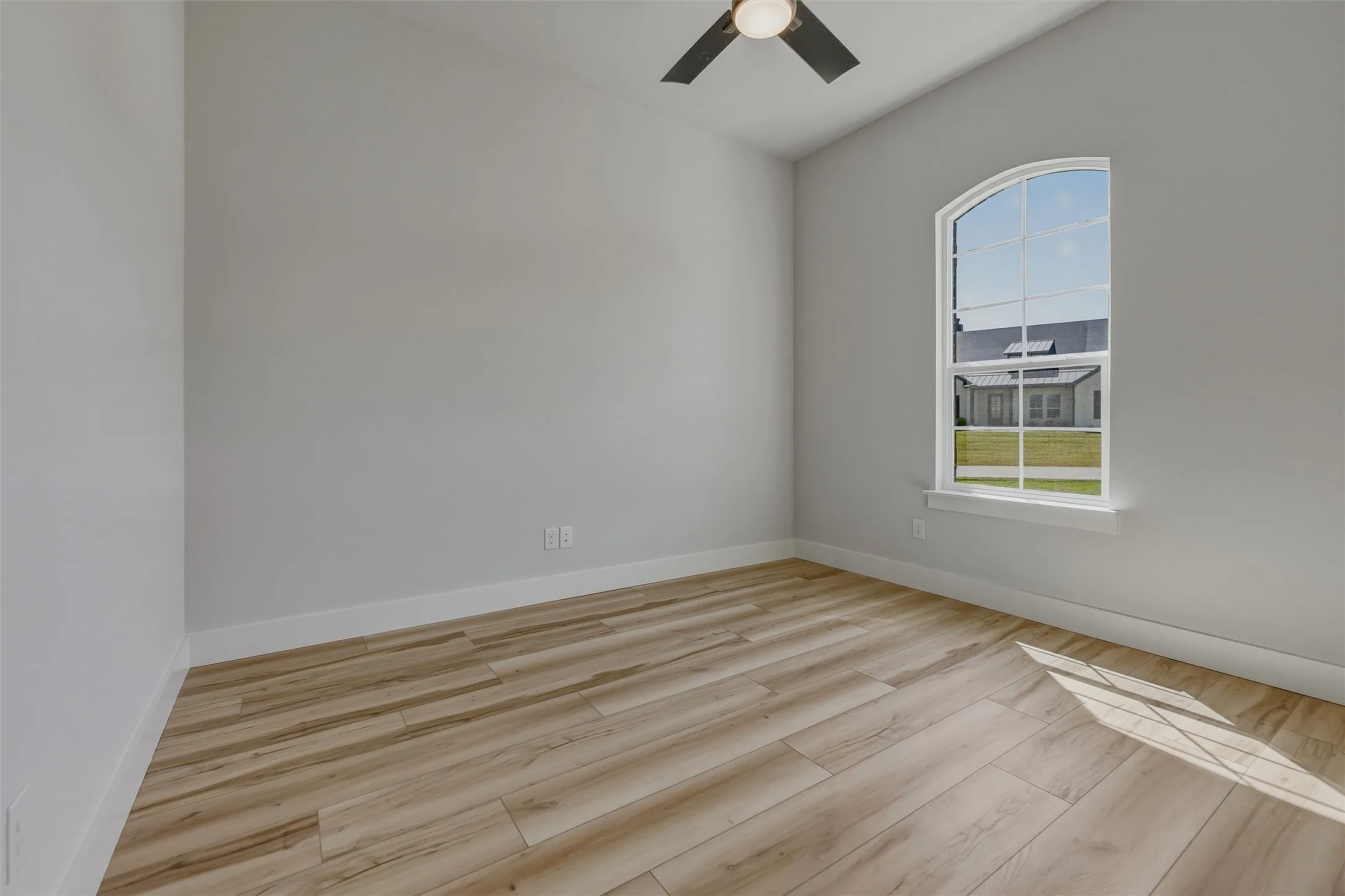 Arched window, wood-finish flooring, ceiling fan, and light gray walls