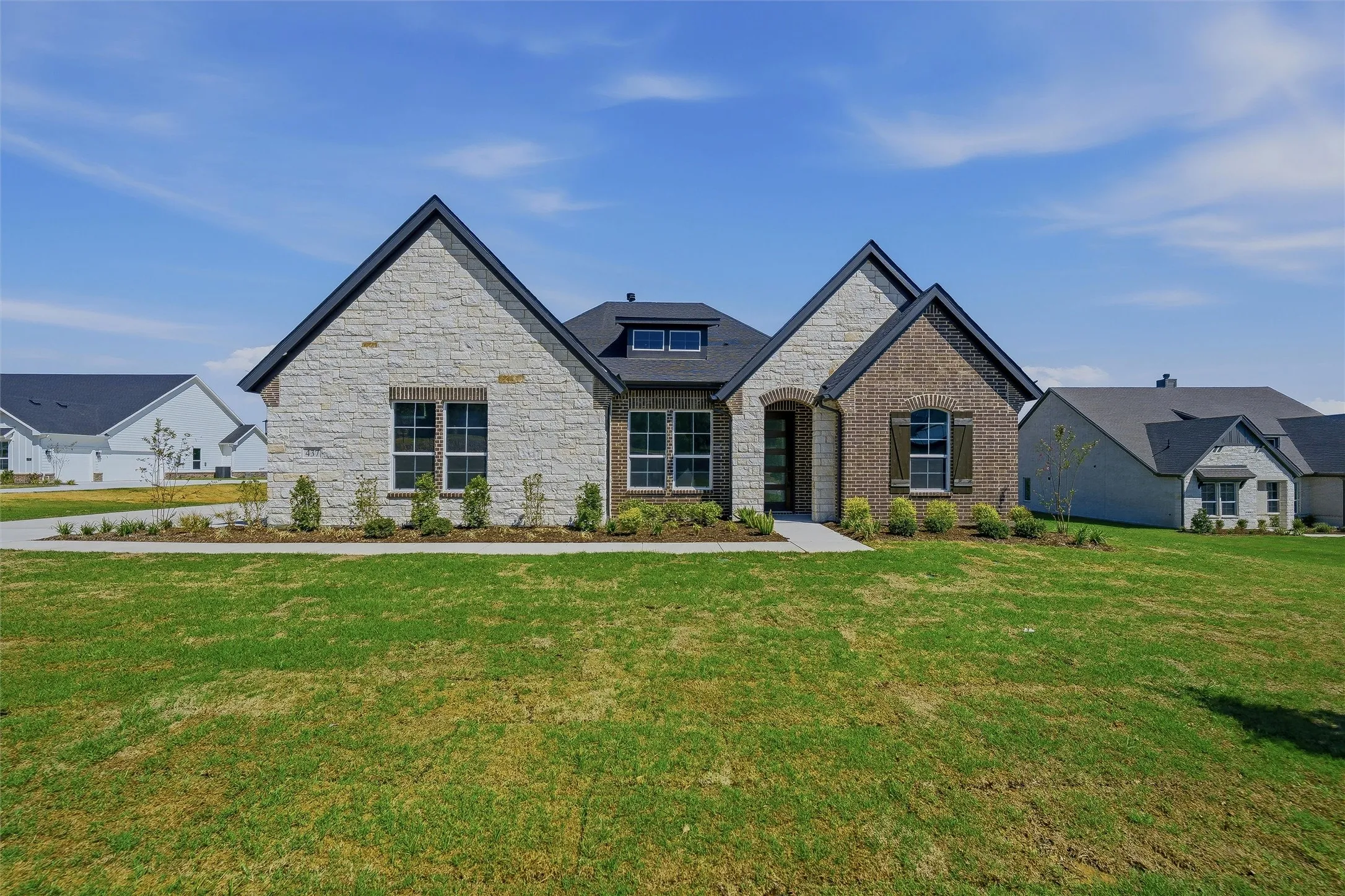Stone and brick facade with dark trim, prominent gables, dark shingle roofing, and a landscaped front yard