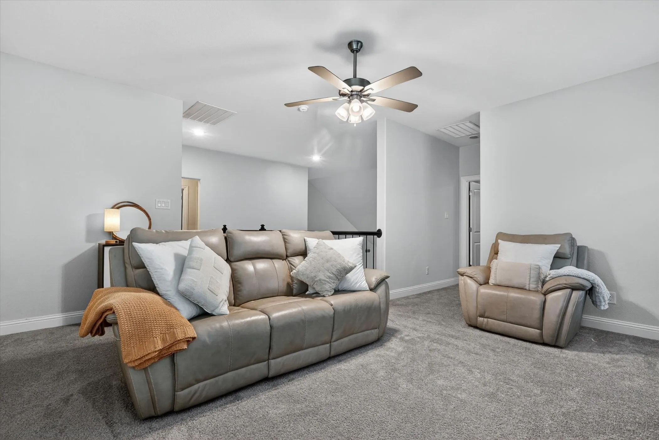 Spacious carpeted room featuring light gray walls, white baseboards, and a ceiling fan with integrated lighting