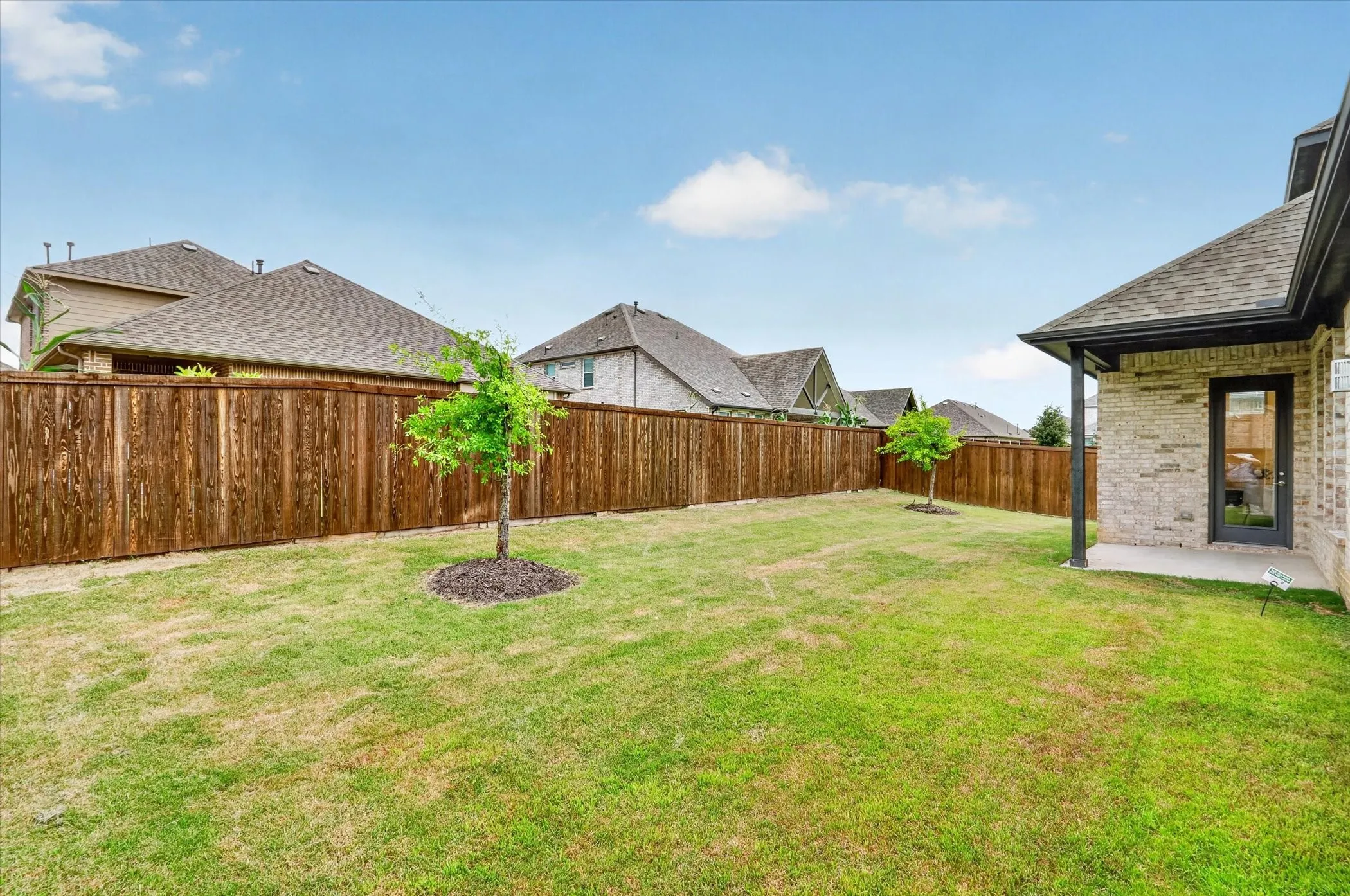 Expansive backyard featuring a manicured lawn, established privacy fencing, and two young trees