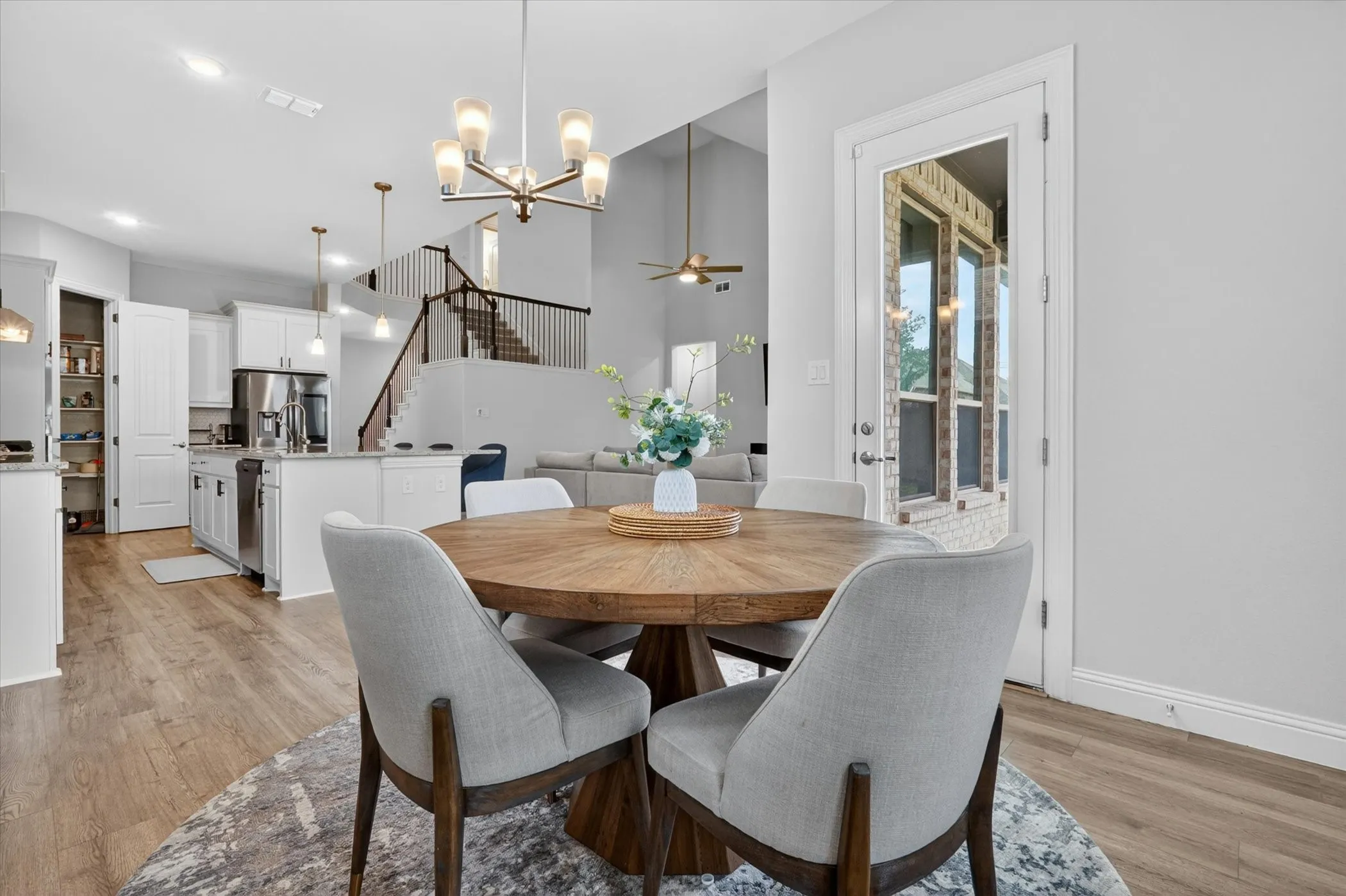 Open-concept living area featuring wood-finish flooring, a contemporary chandelier, a kitchen with white cabinetry and an island, and a staircase with dark railings