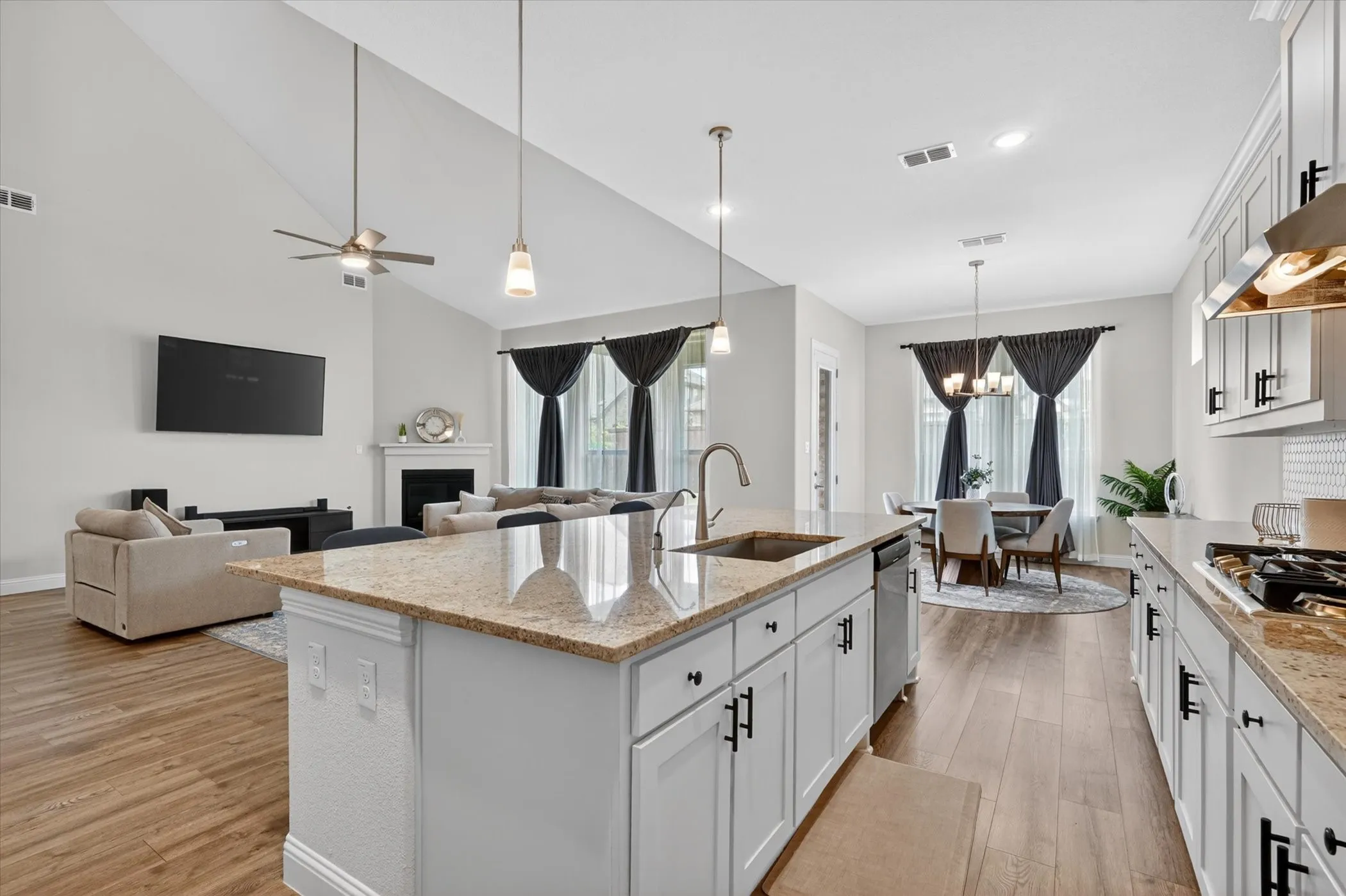 Open-concept living area featuring a kitchen island with sink, white cabinetry with black hardware, wood-finish flooring, and a vaulted ceiling