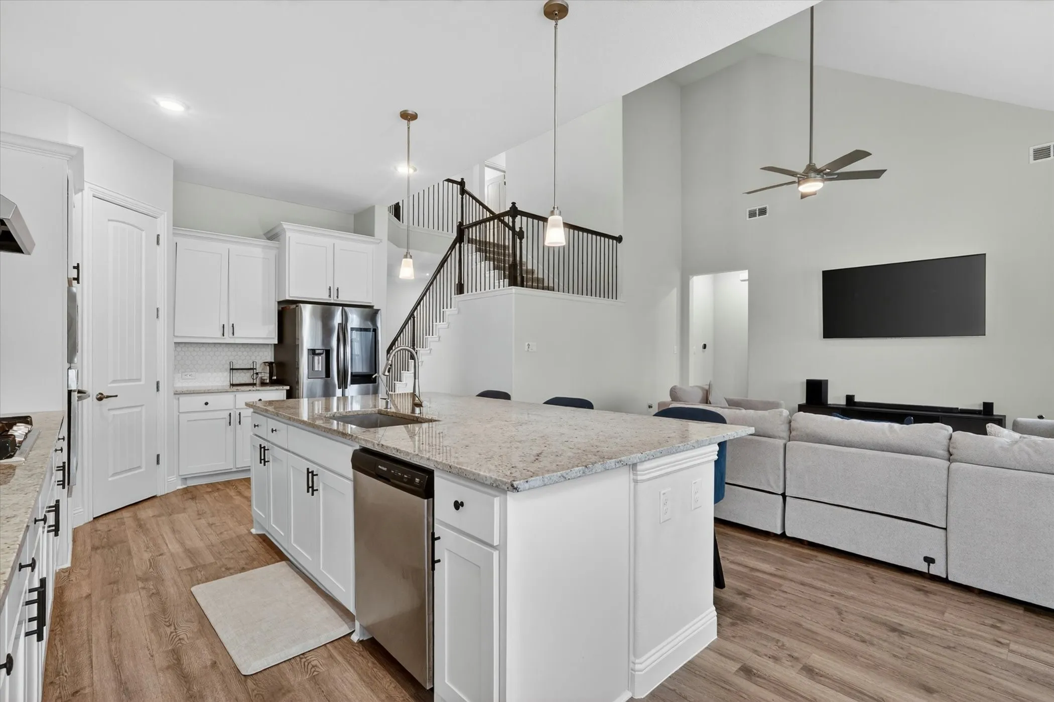 Open-concept kitchen featuring white cabinetry, stainless steel appliances, a large center island with a sink, and granite countertops