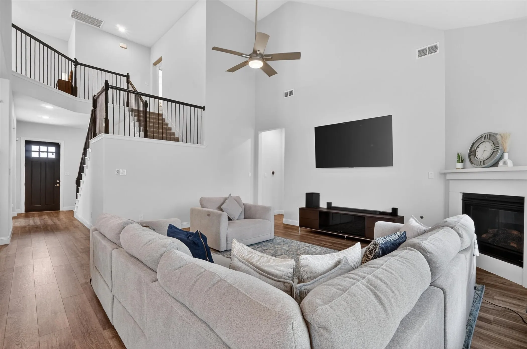 Vaulted ceiling living area featuring a fireplace with a white mantel, wood-finish flooring, and a two-story staircase with dark balusters