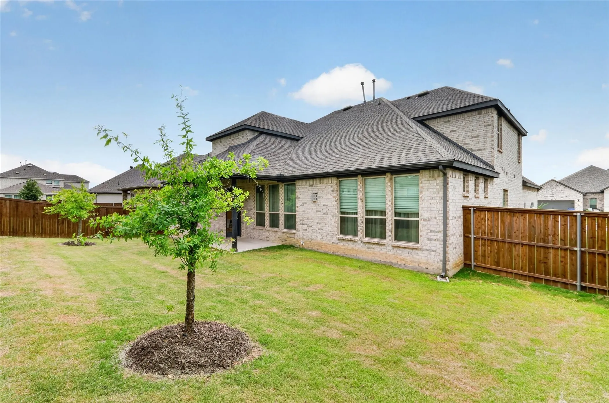 Spacious backyard featuring a manicured lawn, established trees, and a privacy fence