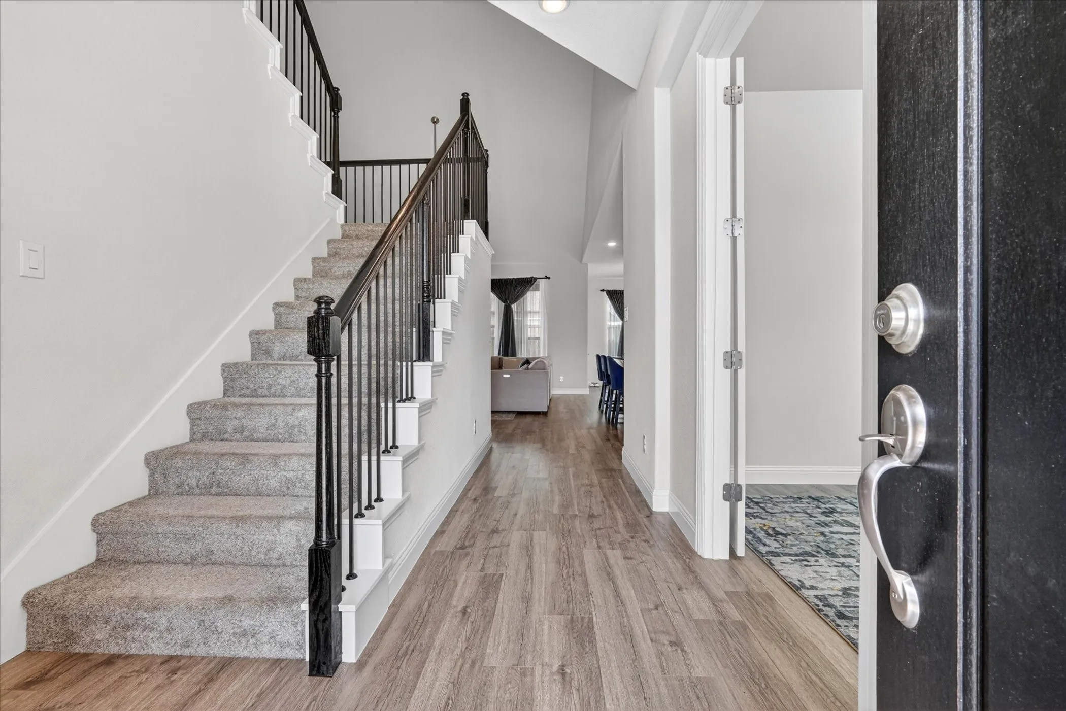 Entry foyer featuring wood-finish flooring, a carpeted staircase with iron balusters, and a vaulted ceiling