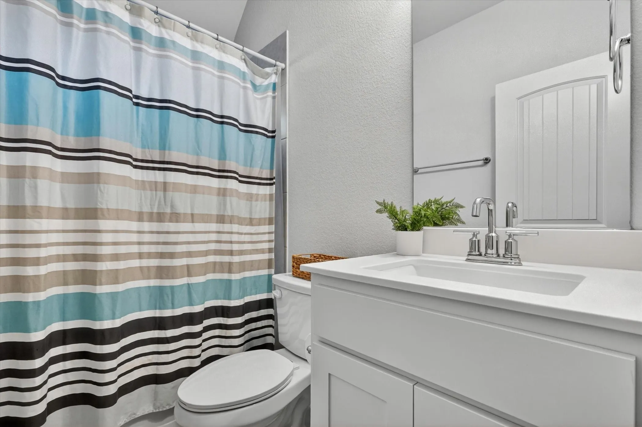 Bathroom featuring a white vanity with integrated sink, chrome faucet, wall-mounted mirror, and toilet