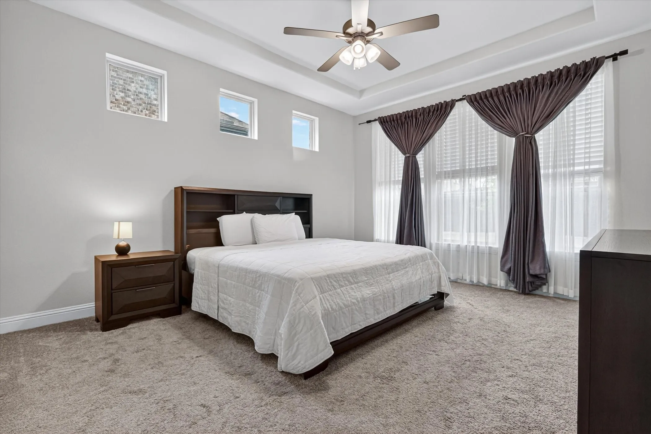 Carpeted bedroom featuring a tray ceiling with a ceiling fan