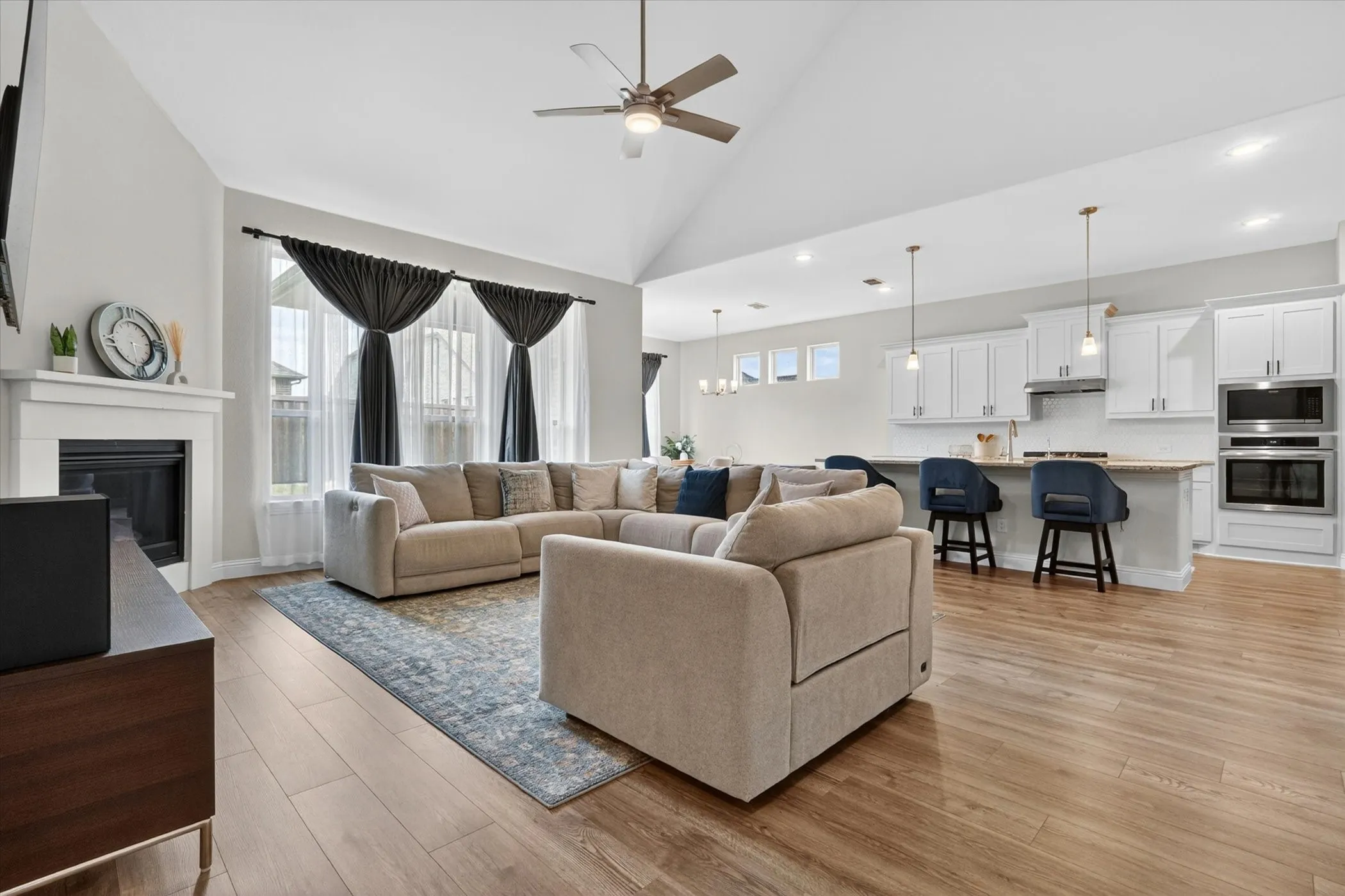 Open-concept living space featuring wood-finish flooring, a vaulted ceiling, and a fireplace with a white mantel