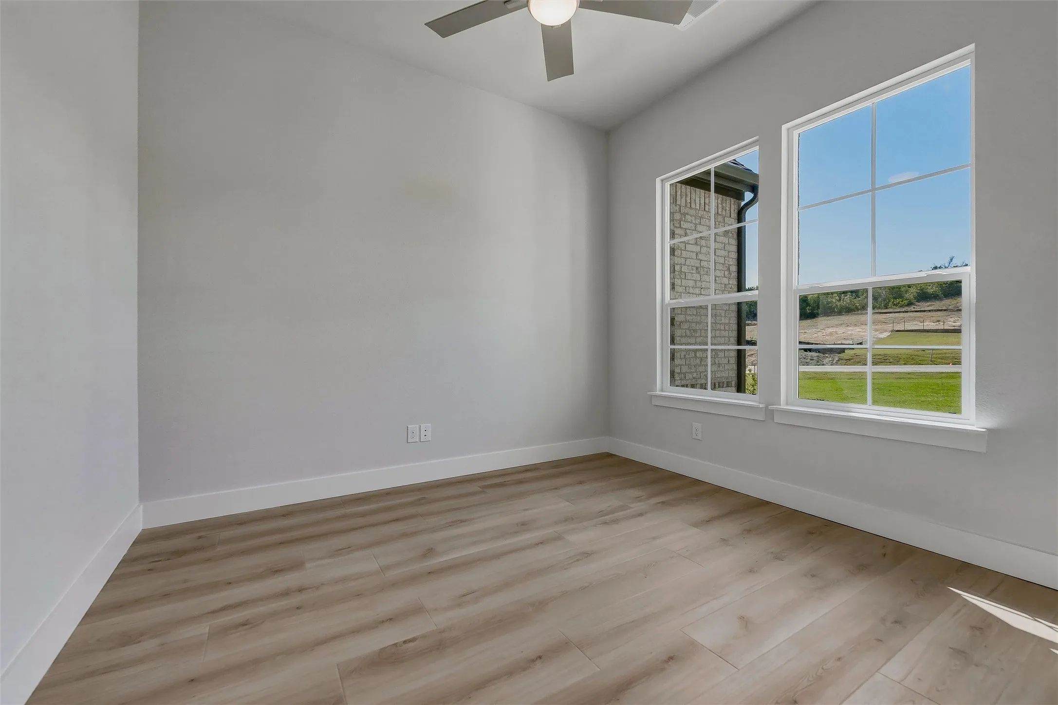 Light wood-finish flooring, dual windows, and a ceiling fan with integrated lighting