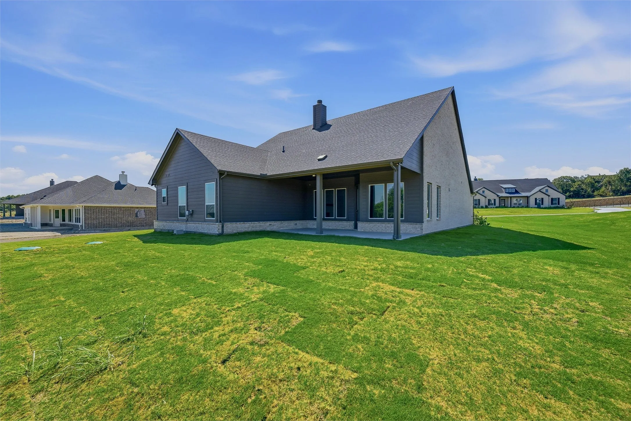 Expansive green space featuring a covered patio, multiple large windows, and a dark shingle roof