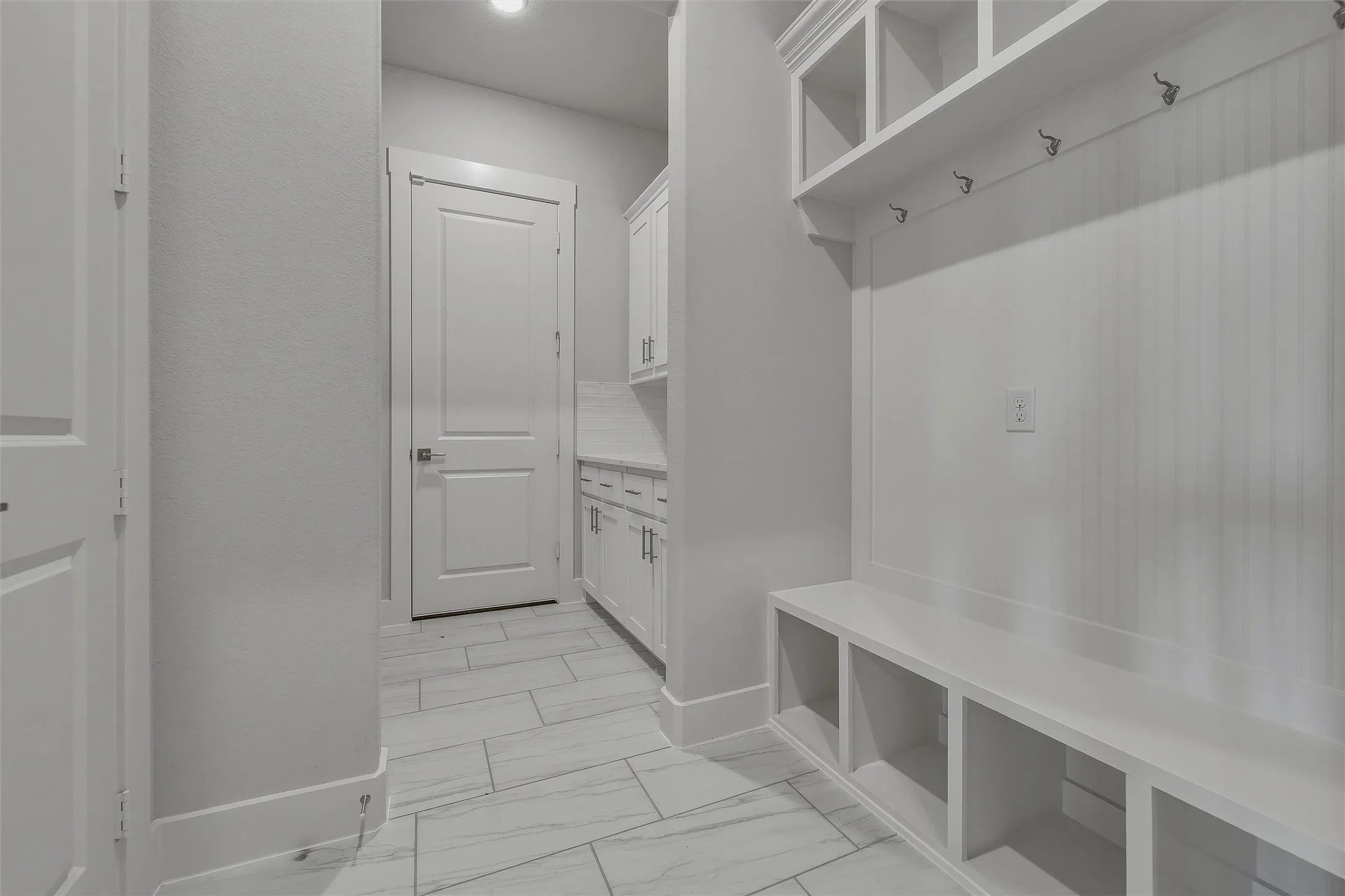 Built-in cubbies and coat hooks, white cabinetry, tile flooring, and white interior doors