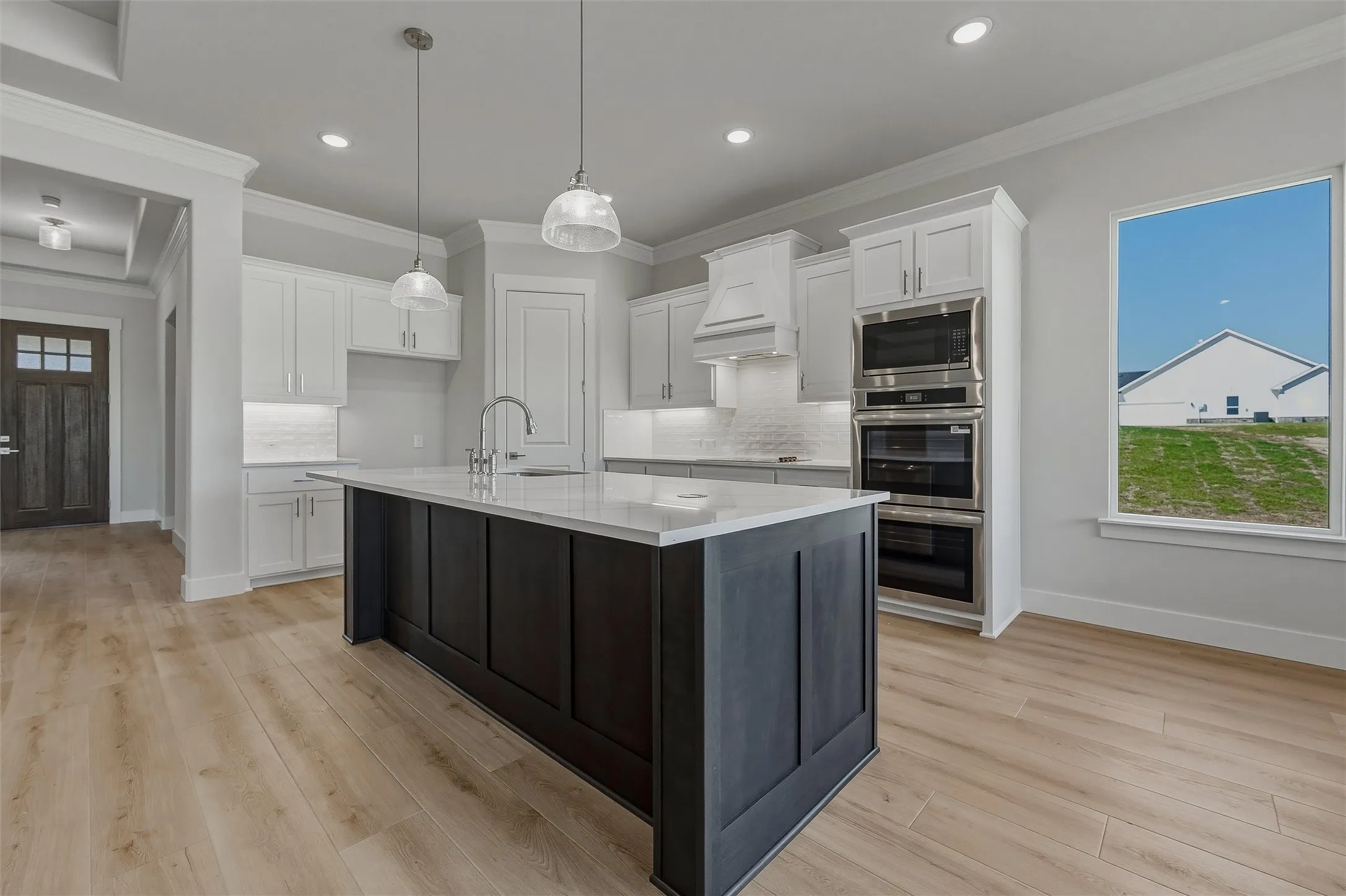 Spacious kitchen featuring a dark-toned island with a light countertop, white perimeter cabinetry, stainless steel double wall ovens, and wood-finish flooring