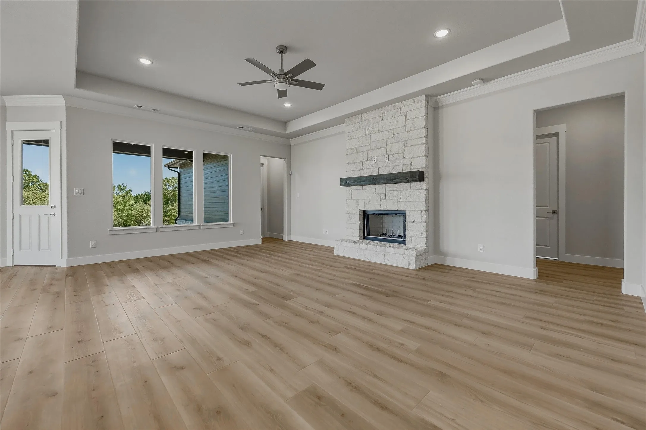 Spacious room featuring wood-finish flooring, a stone-clad fireplace with a dark wood mantel, recessed lighting, a ceiling fan, and multiple windows