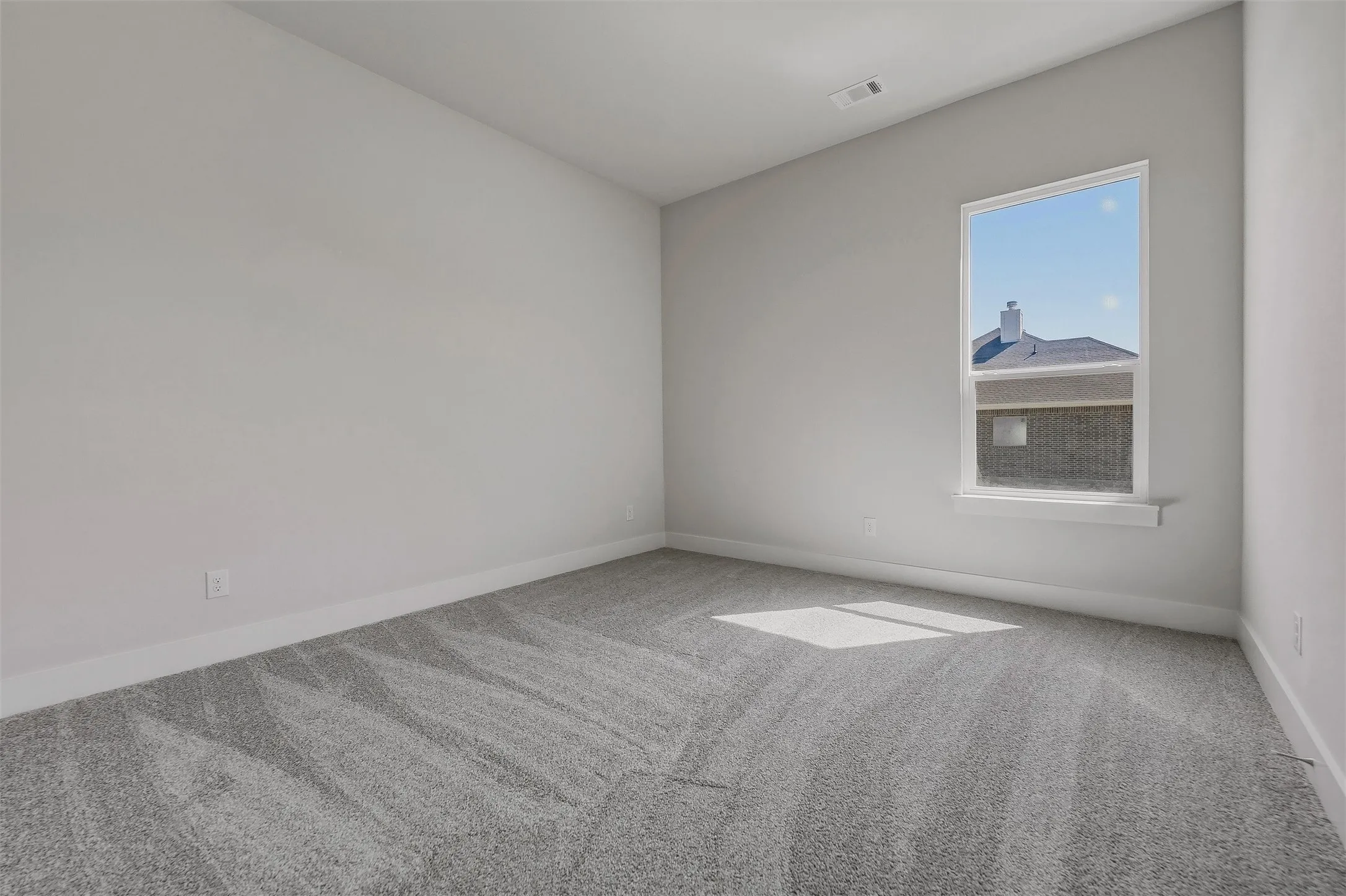 Light gray wall paint, gray patterned carpet, and a single window with white trim