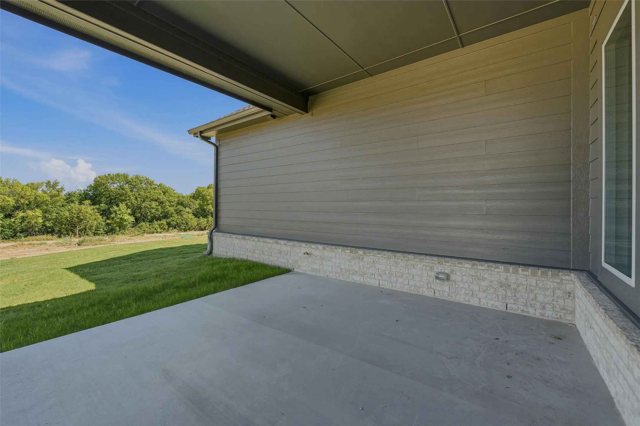Expansive concrete patio with an overhead soffit, complemented by horizontal siding and a stone veneer foundation